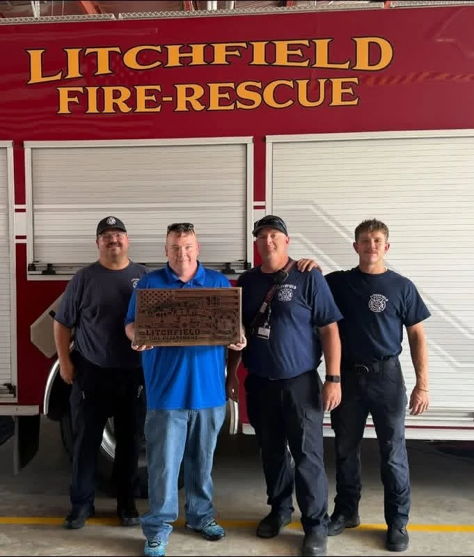 Four men stand in front of a red fire truck labeled 'Litchfield Fire-Rescue'; one holds a plaque.