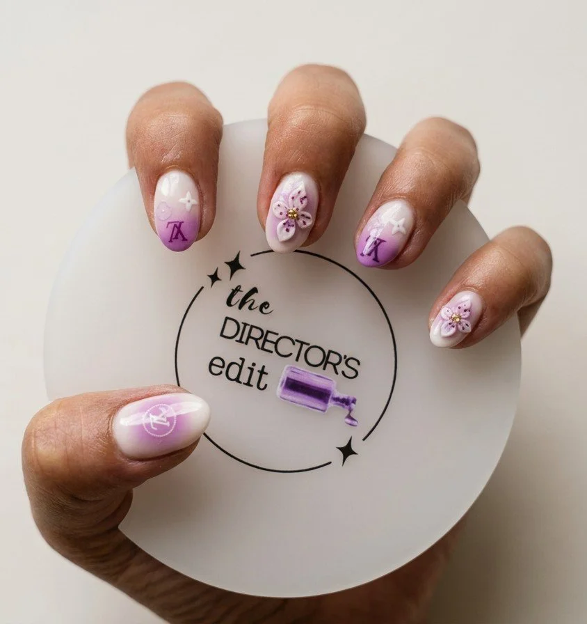 Hand with custom lavender floral press-on nails holding a The Director's Edit logo disc