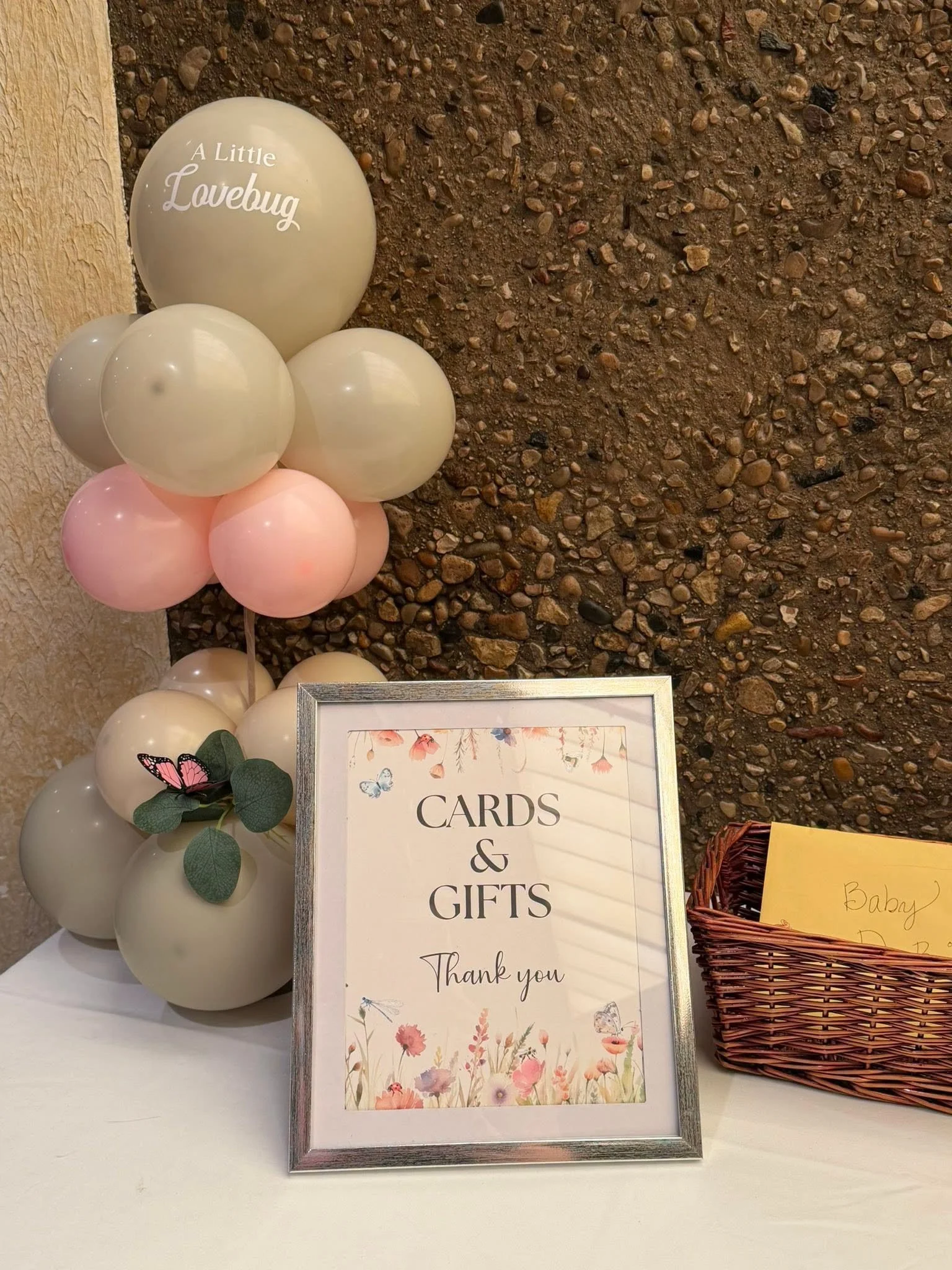 Baby shower gift table with pastel balloons, a framed “Cards & Gifts” sign, and a wicker card basket.
