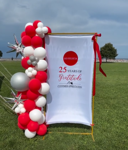 Outdoor 25 years of gratitude customer appreciation banner decorated with red, white, and silver balloons and starbursts on a lawn