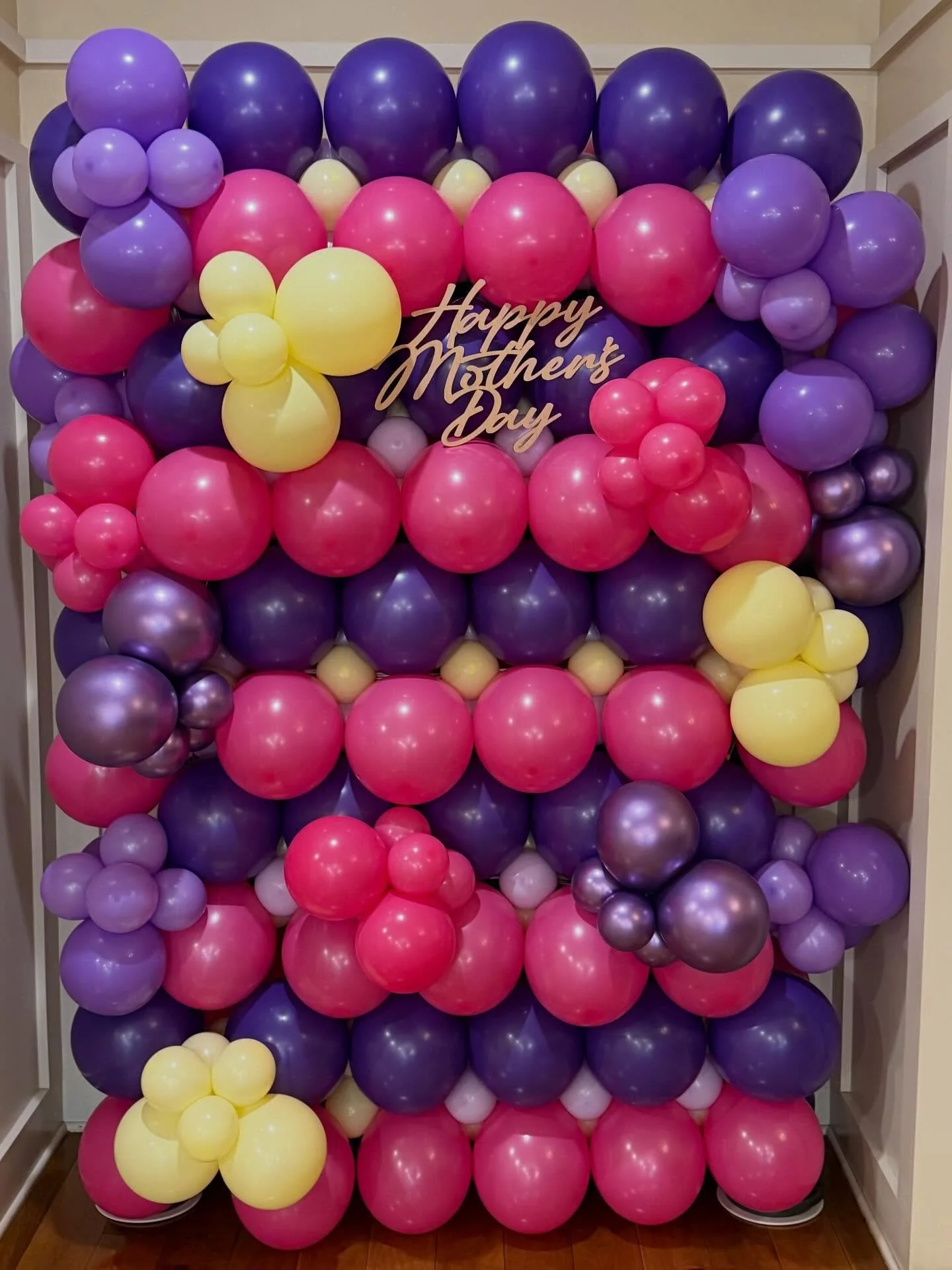 Colorful pink, purple, and yellow balloon wall with flowers and a “Happy Mother’s Day” sign