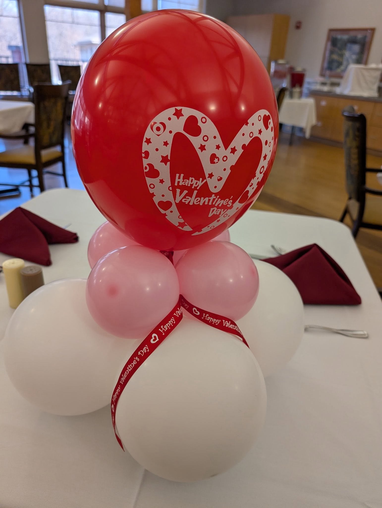 Valentine’s Day balloon centerpiece with a red heart-patterned balloon, pink and white balloons, and red ribbon on a restaurant table
