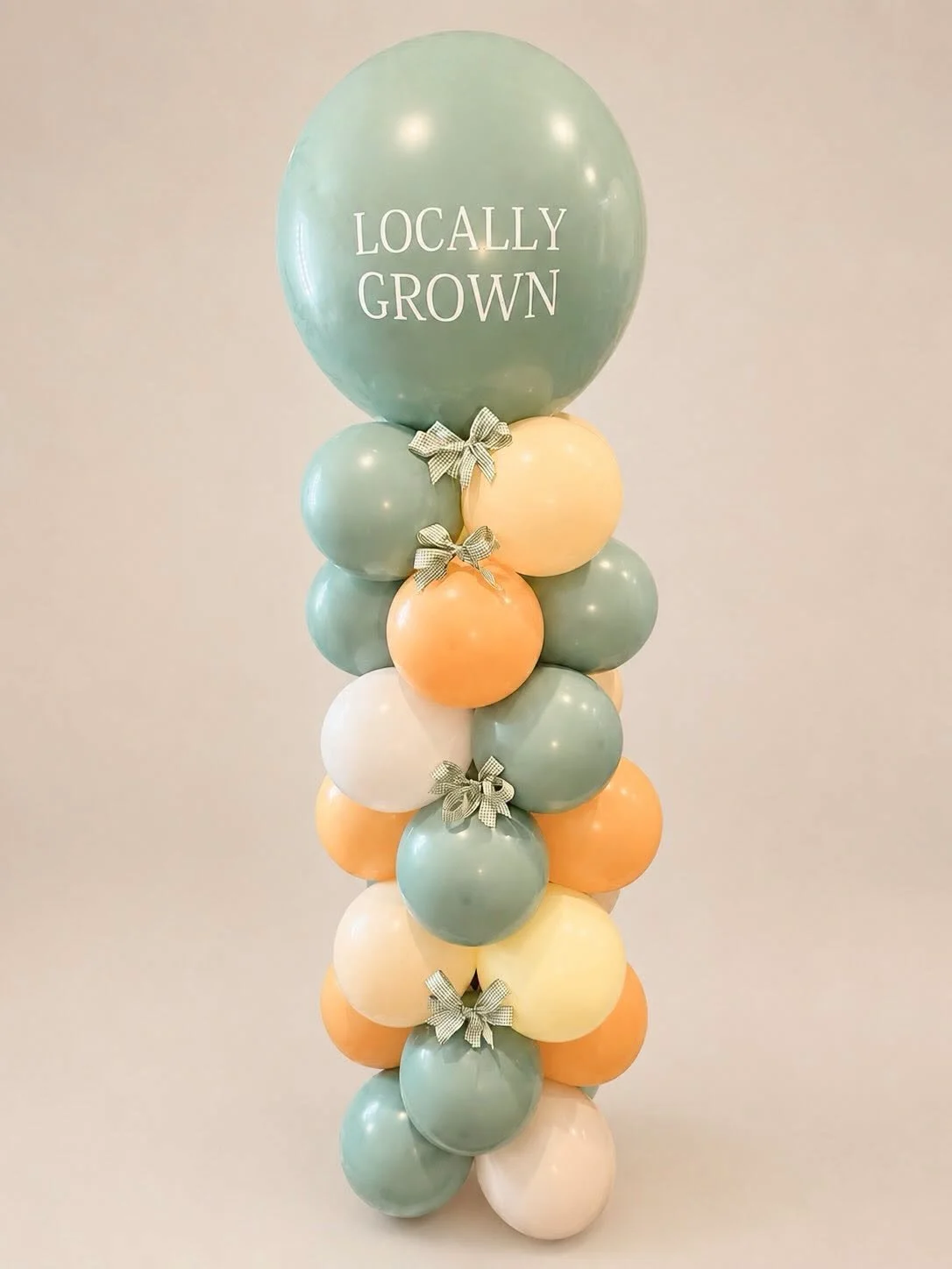 Pastel green, orange, yellow, and white balloon arrangement with bows and a large balloon reading “Locally Grown.”