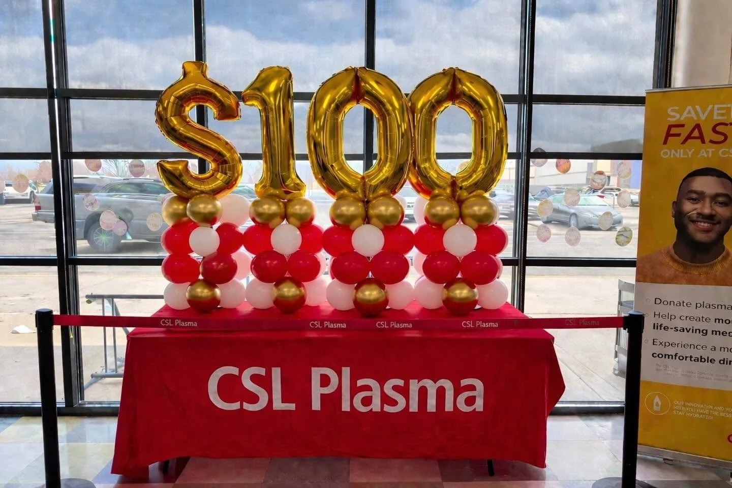 CSL Plasma anniversary display featuring gold “1000” balloon numbers and red, white, and gold balloon arrangements on a branded table.