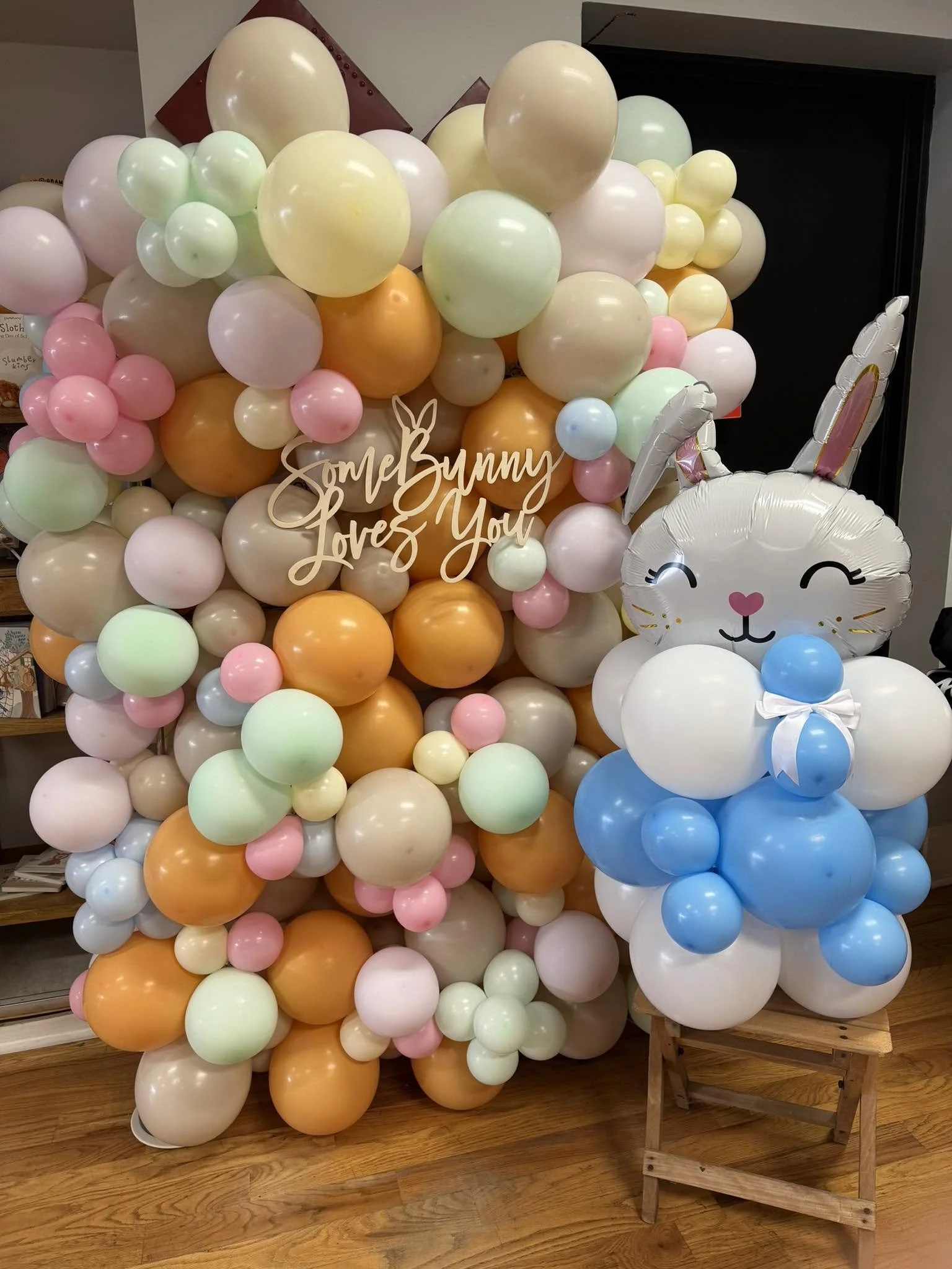 Pastel balloon display with a smiling bunny balloon and script sign reading “Some Bunny Loves You.”