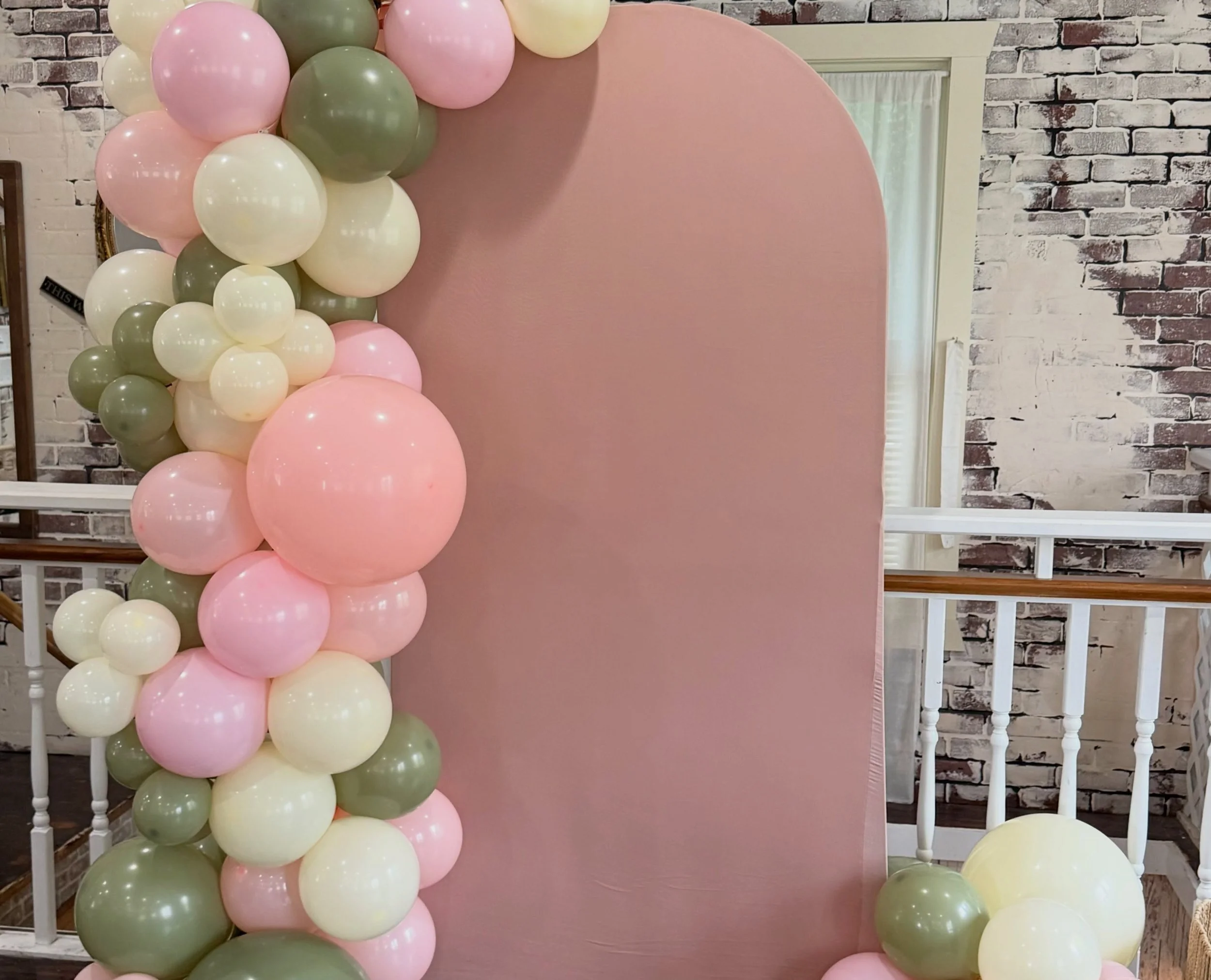 Pink photo backdrop decorated with pastel pink, cream, and sage green balloon garlands