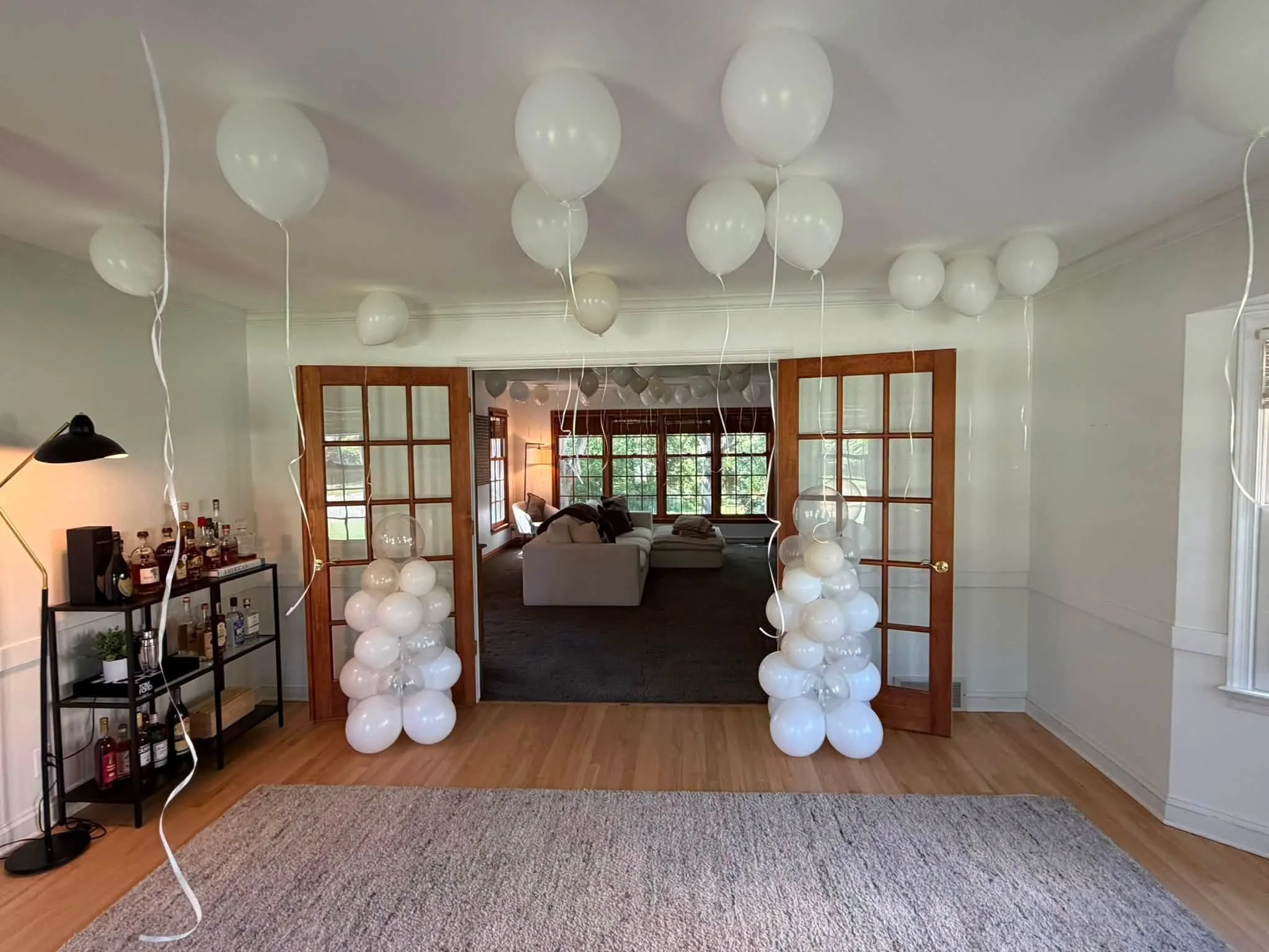 Living room decorated with white balloons, balloon columns, wood-framed French doors, and a home bar