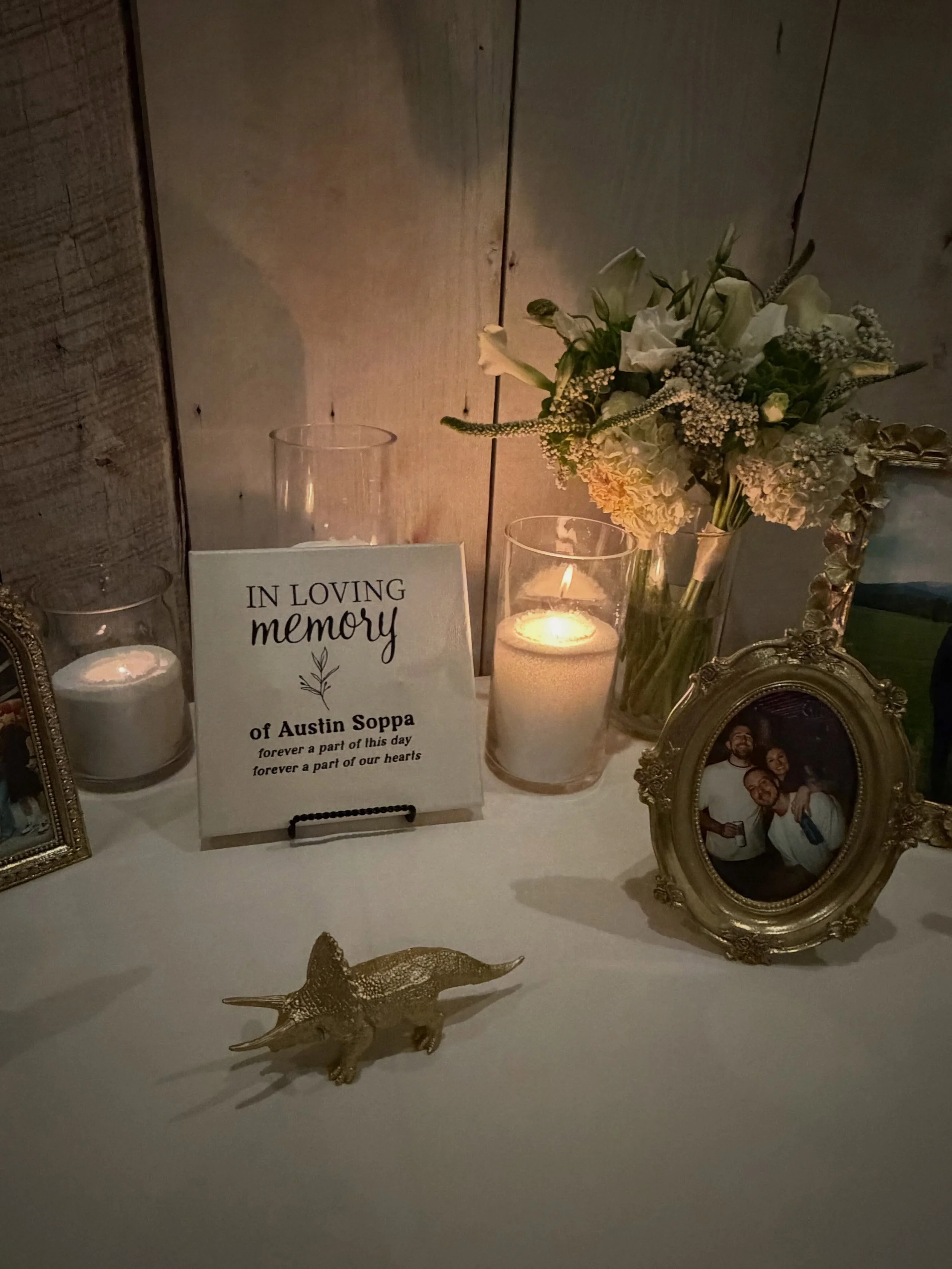 Memorial display with lit candles, white flower arrangement, framed family photos, and an “In Loving Memory” sign for Austin Soppa.