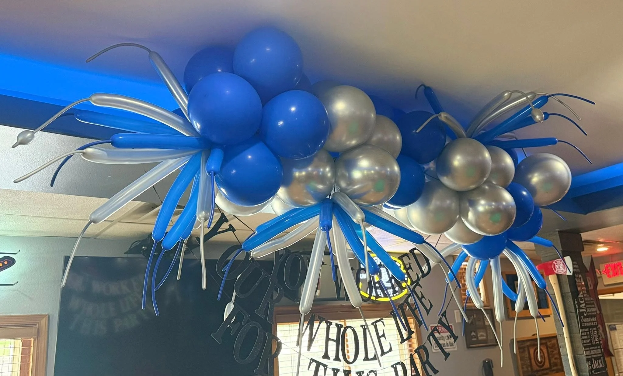 Blue, silver, and white balloon garland with long balloon accents decorating a bar or restaurant ceiling