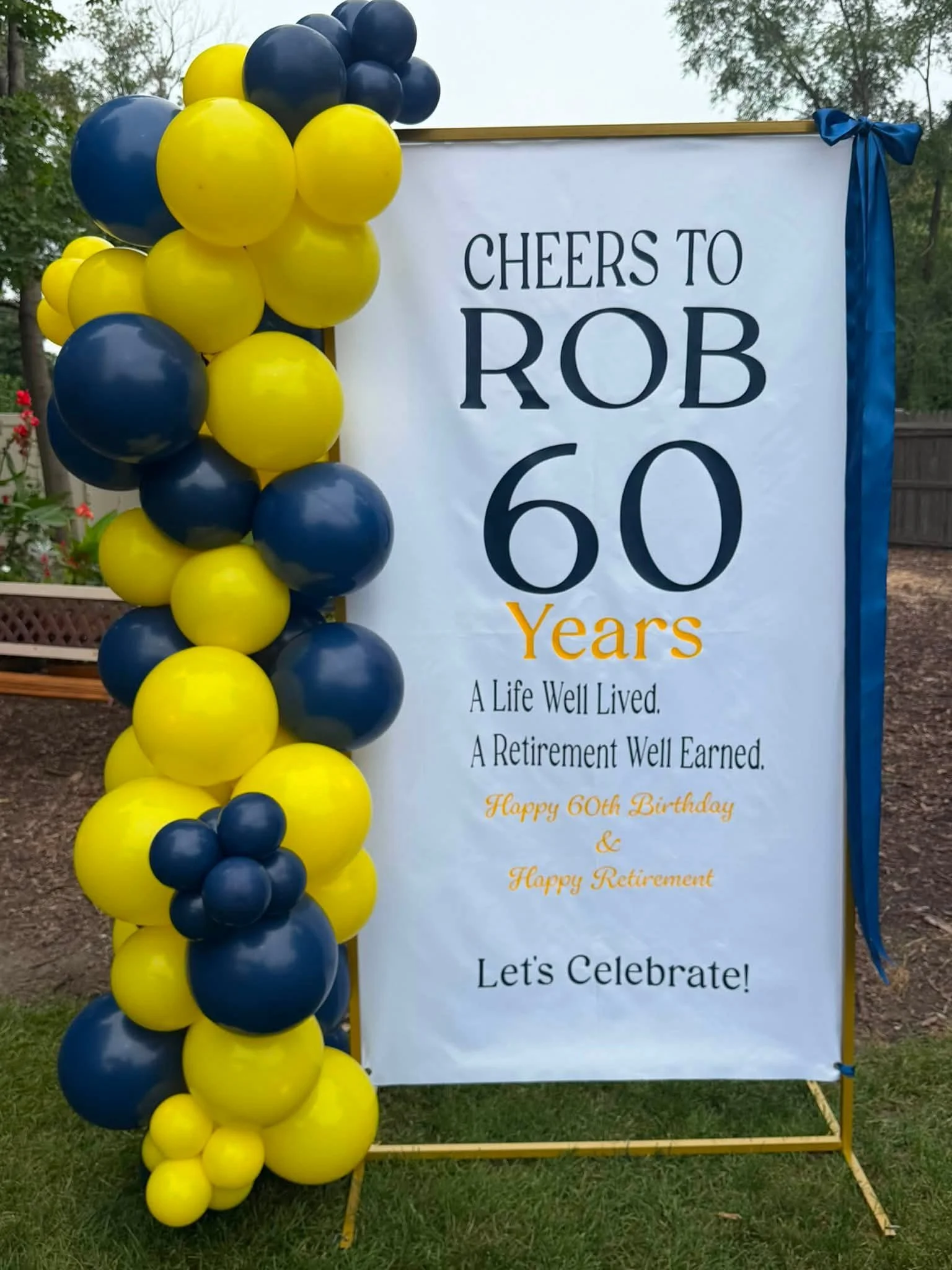 Blue and yellow balloon display beside a sign celebrating Rob's 60th birthday and retirement.