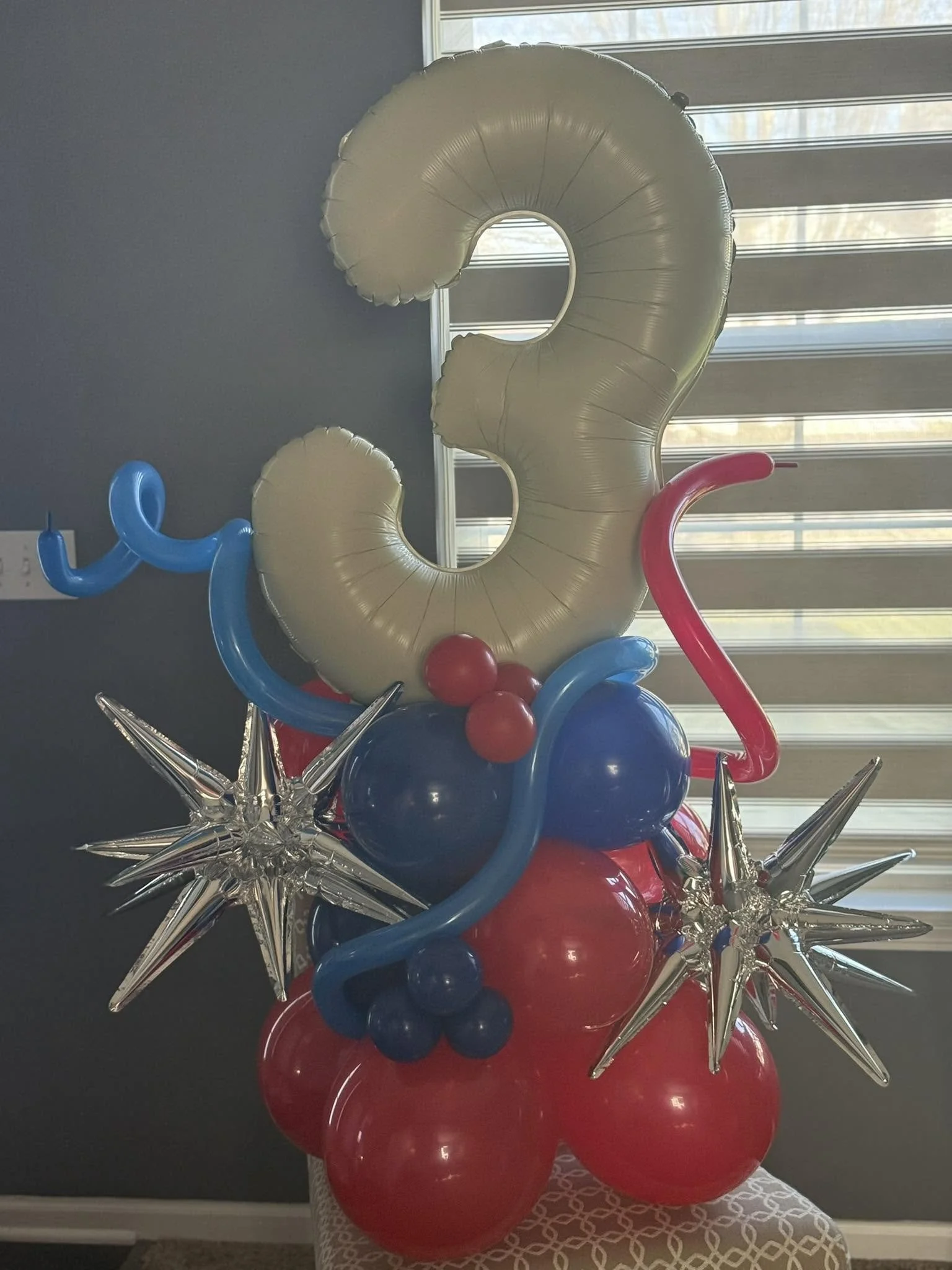 Colorful balloon sculpture with a large gold number three, red and blue balloons, and silver starburst accents.