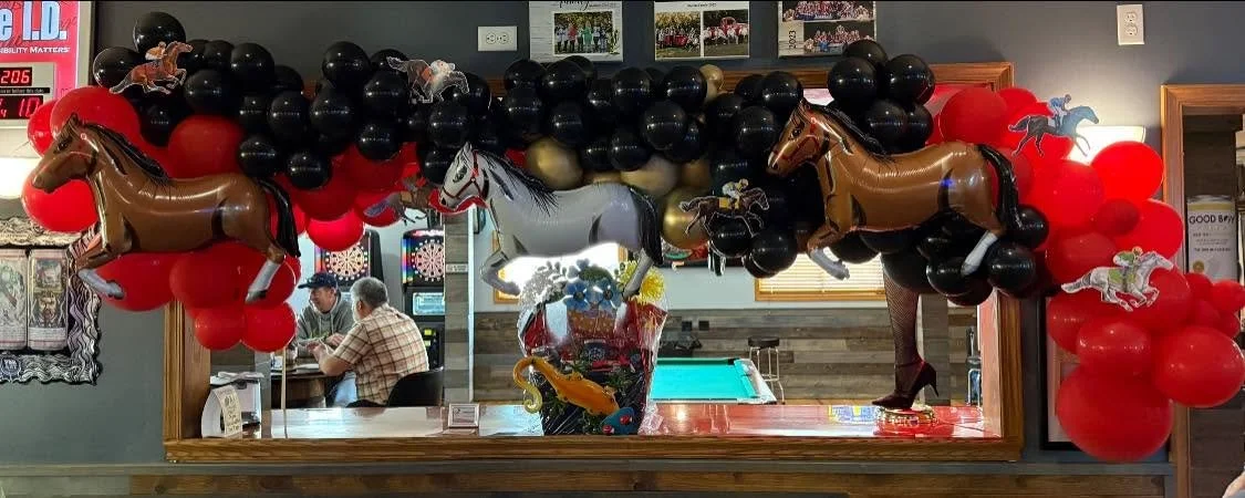 Horse-themed balloon arch with red, black, and gold balloons decorating a bar mirror.
