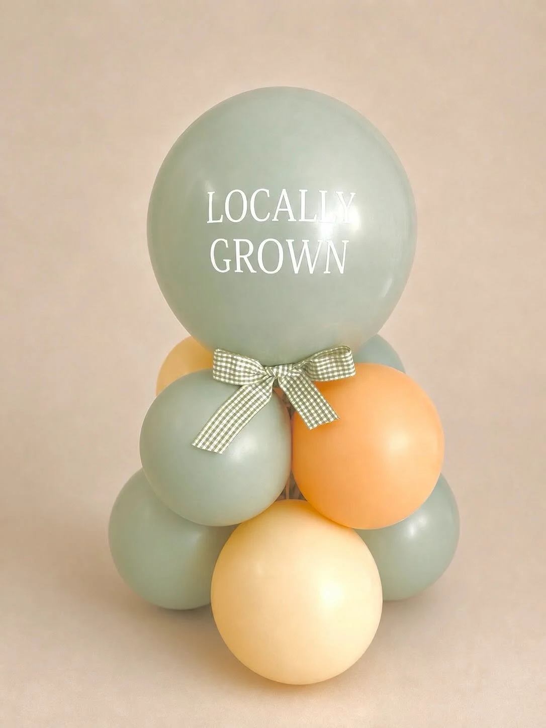 Pastel green, orange, and cream balloon arrangement with a gingham bow and “LOCALLY GROWN” lettering.