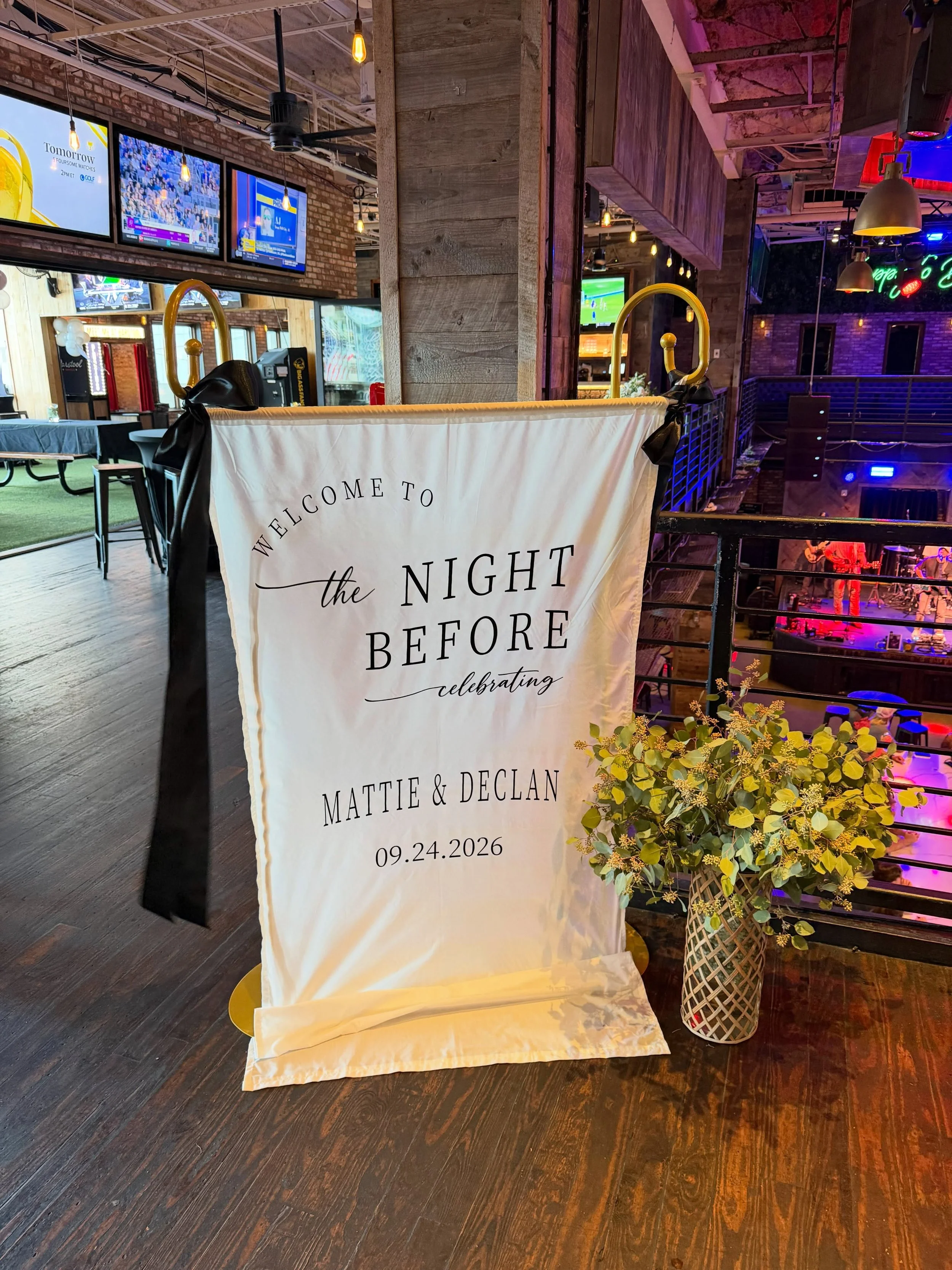 Wedding welcome sign for Mattie and Declan dated September 24, 2026, displayed in a colorful sports bar with televisions and a live music stage.