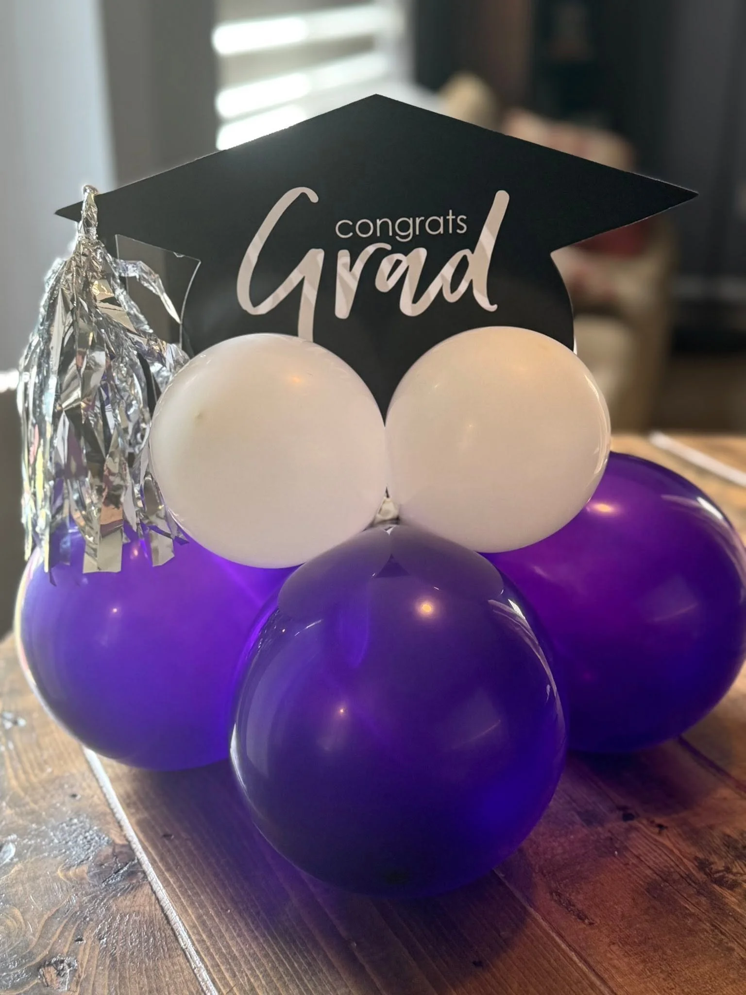 Purple and white balloon graduation arrangement with a black cap reading “Congrats Grad” and silver tassel