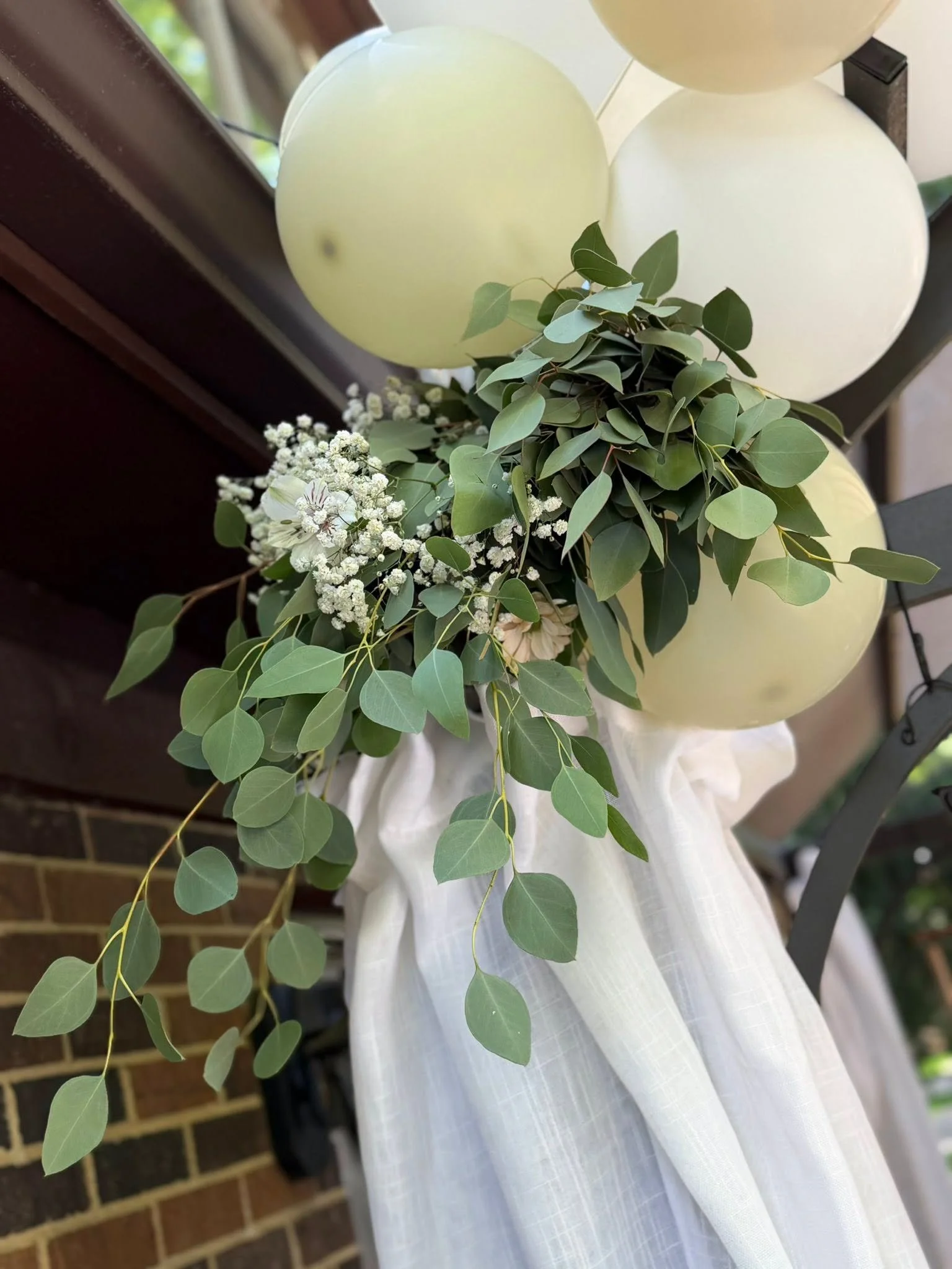 Bride in a white dress holding a greenery bouquet with white flowers, surrounded by cream balloons.