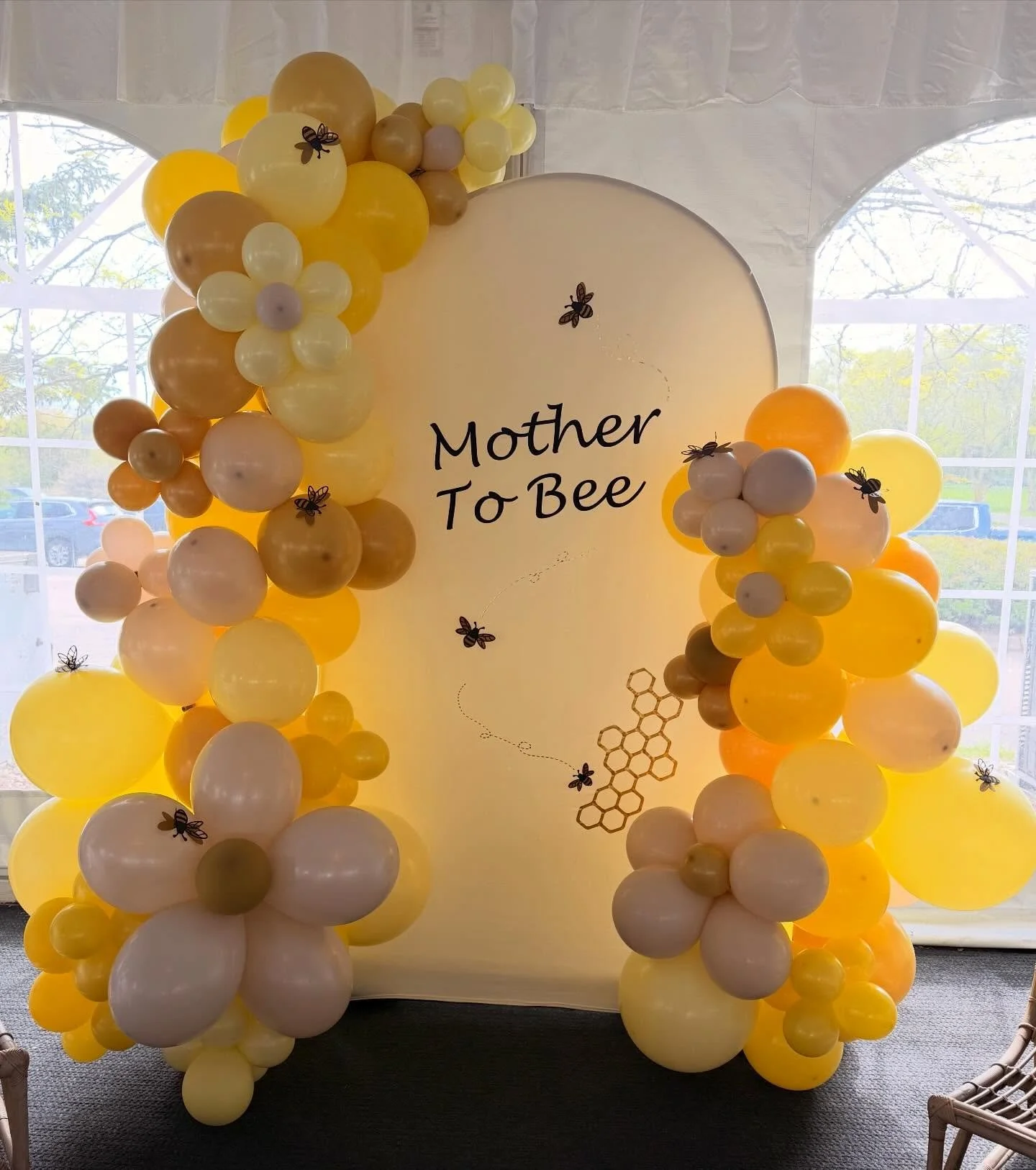 Yellow and cream balloon arch with bee decorations and “Mother To Bee” baby shower sign