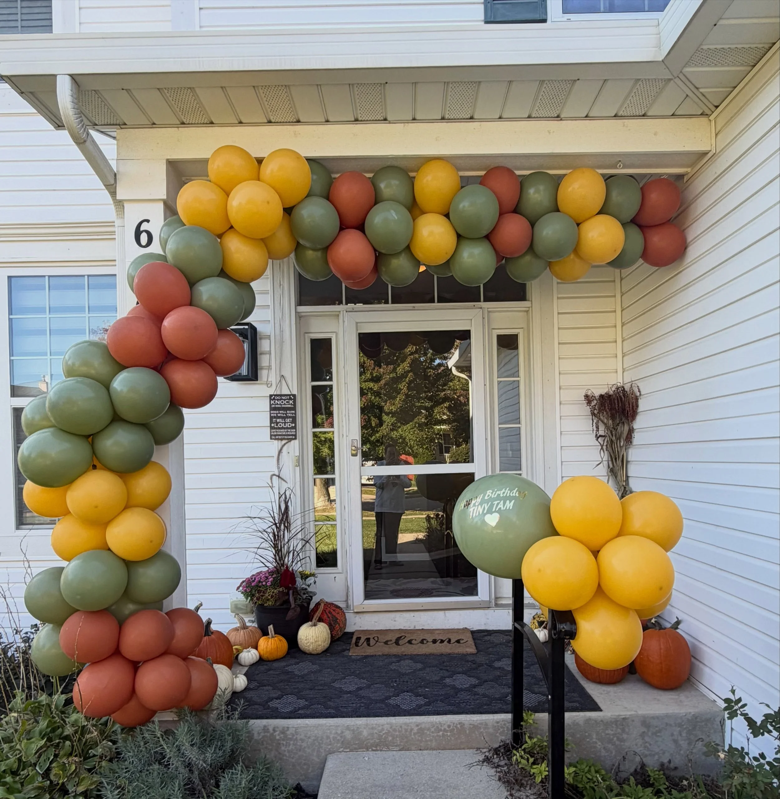 Front porch decorated with a colorful fall balloon arch, pumpkins, and a birthday balloon arrangement.