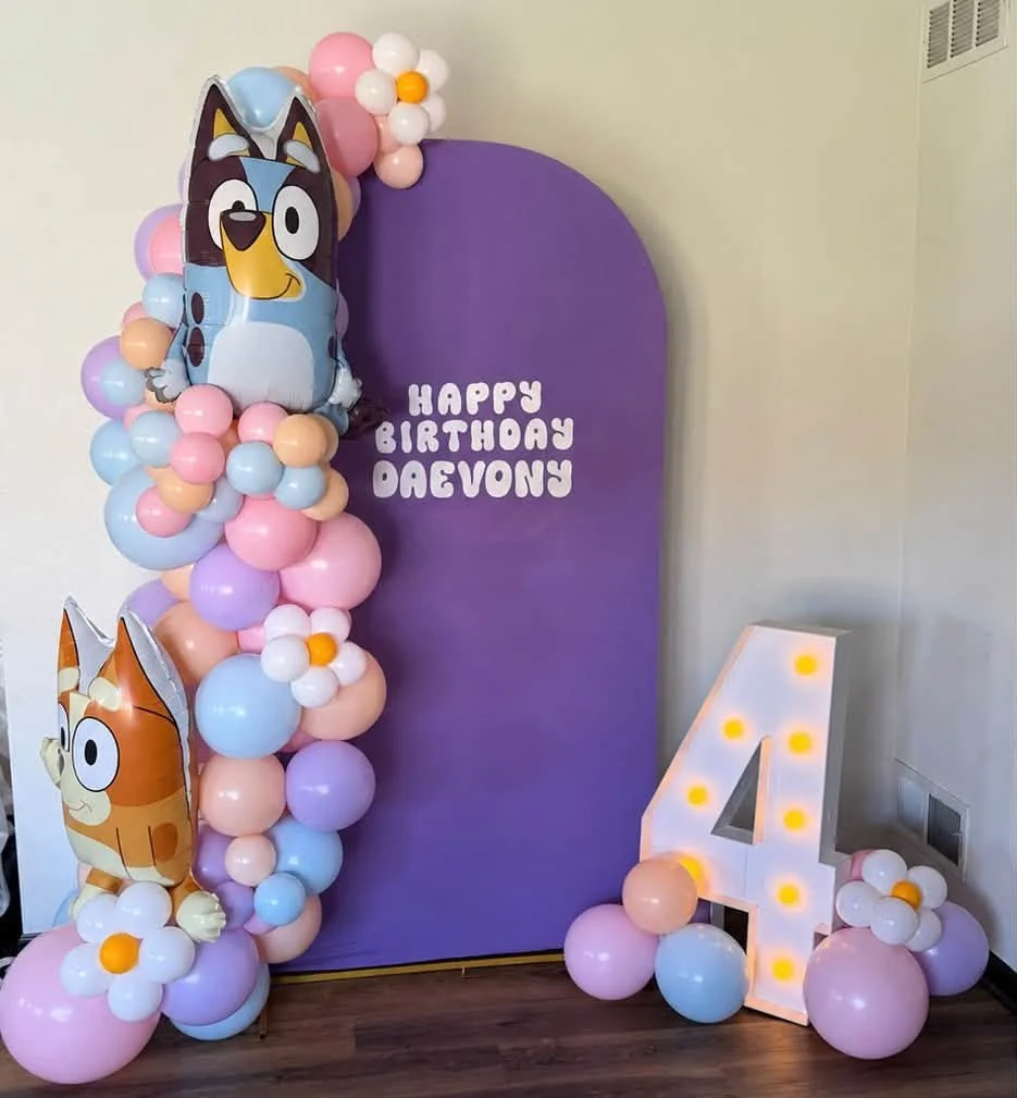 Bluey-themed fourth birthday decoration with pastel balloon garland, character balloons, purple backdrop, and illuminated number 4