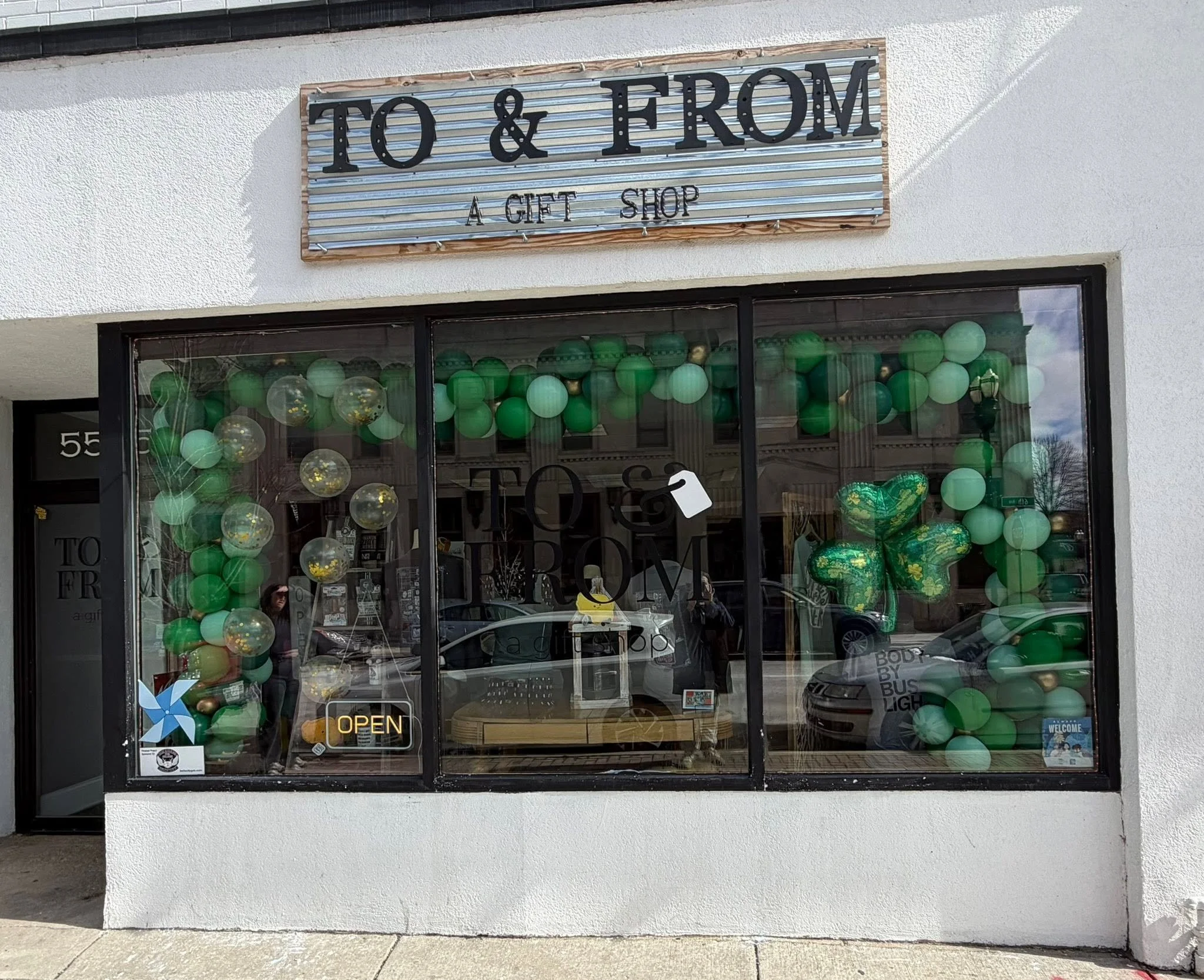 Storefront sign reading “TO & FROM A GIFT SHOP” above a window display filled with green balloons and gifts.