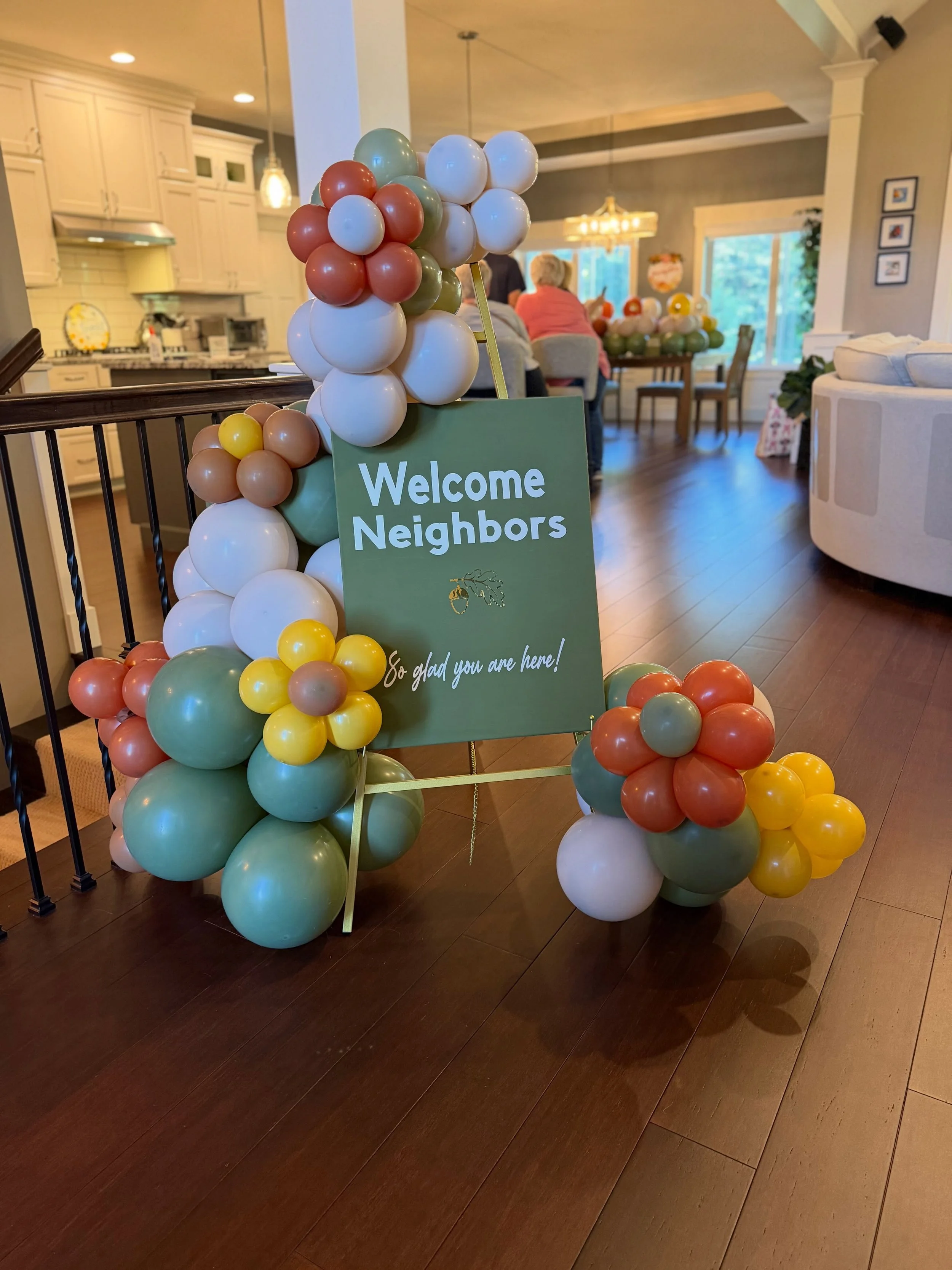 Colorful balloon arch surrounding a green “Welcome Neighbors” sign in a home decorated for a gathering.