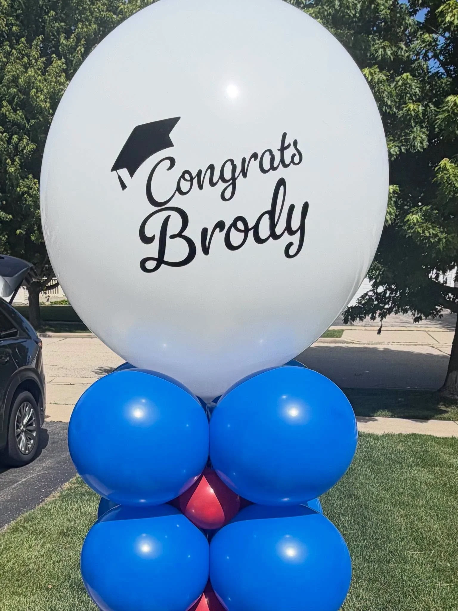 Blue and red graduation balloon arrangement with a large white balloon reading “Congrats Brody” and a graduation cap graphic.