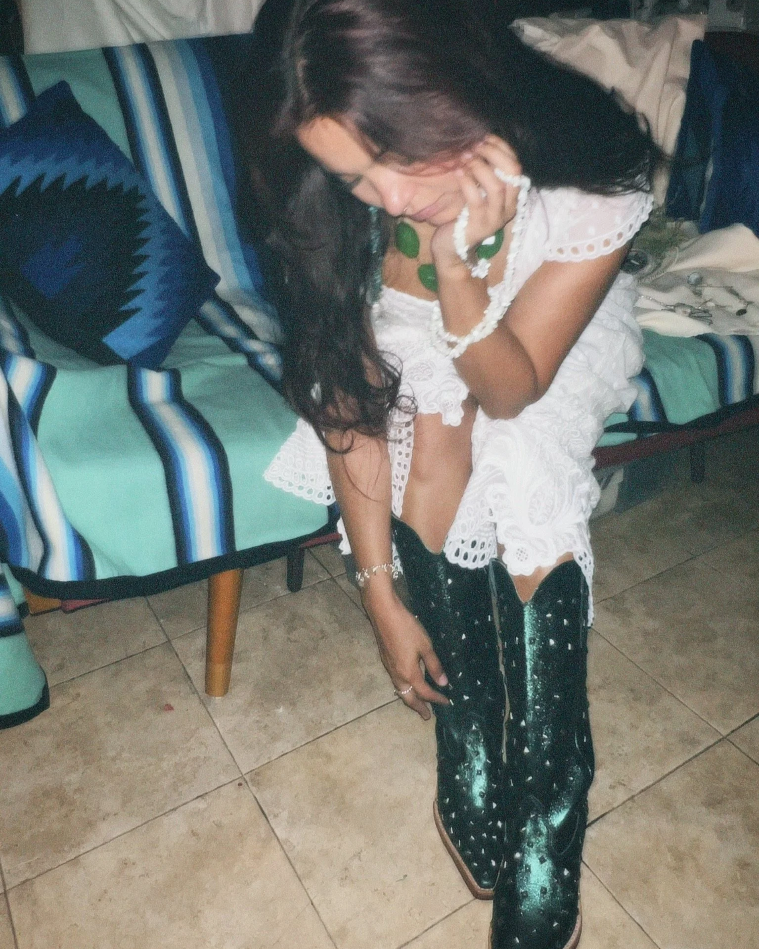 Woman in a white lace dress and glittery black boots sitting on a striped lounge chair indoors