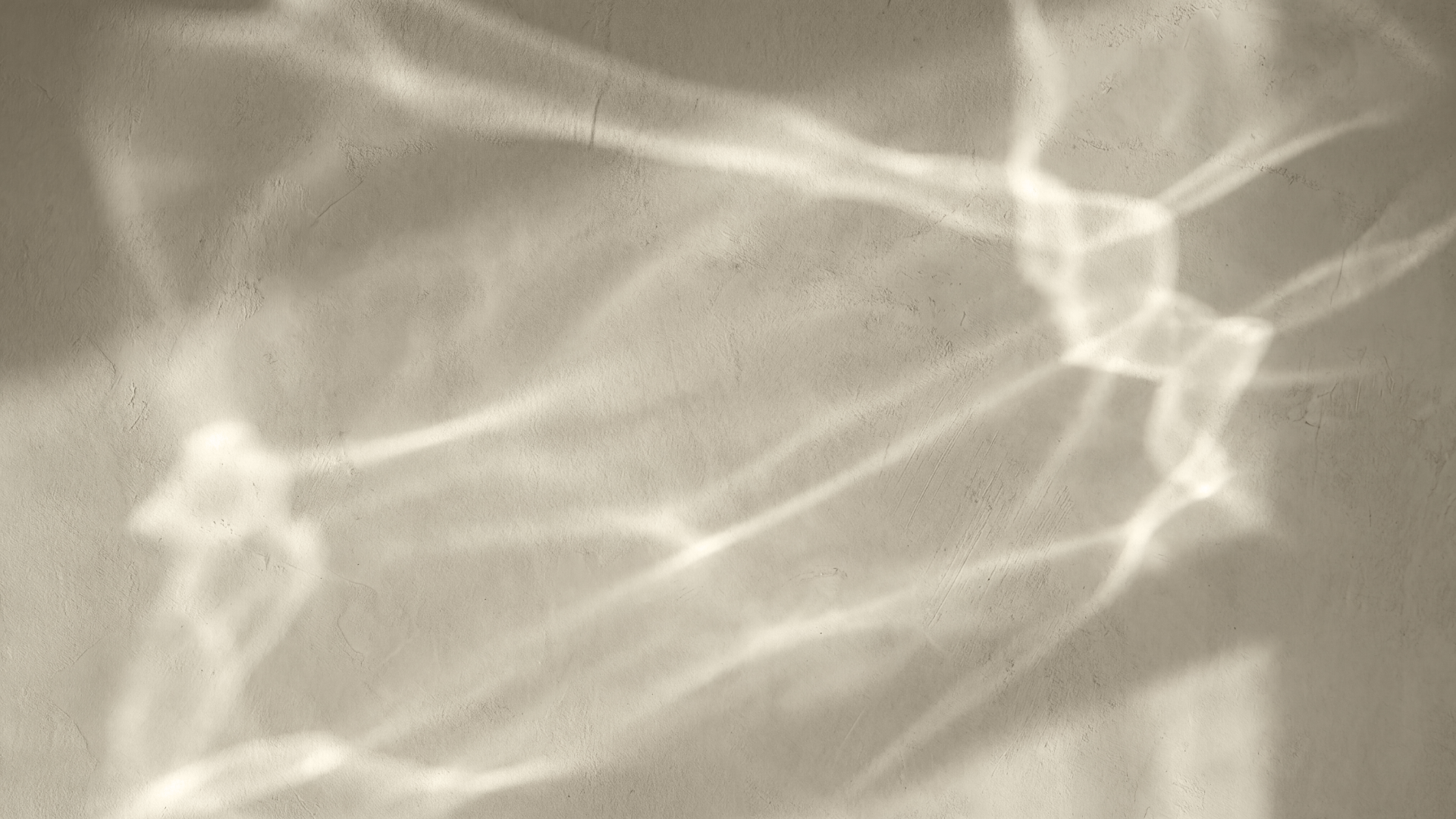 Sunlight shining through a window, creating abstract light and shadow patterns on a beige wall.