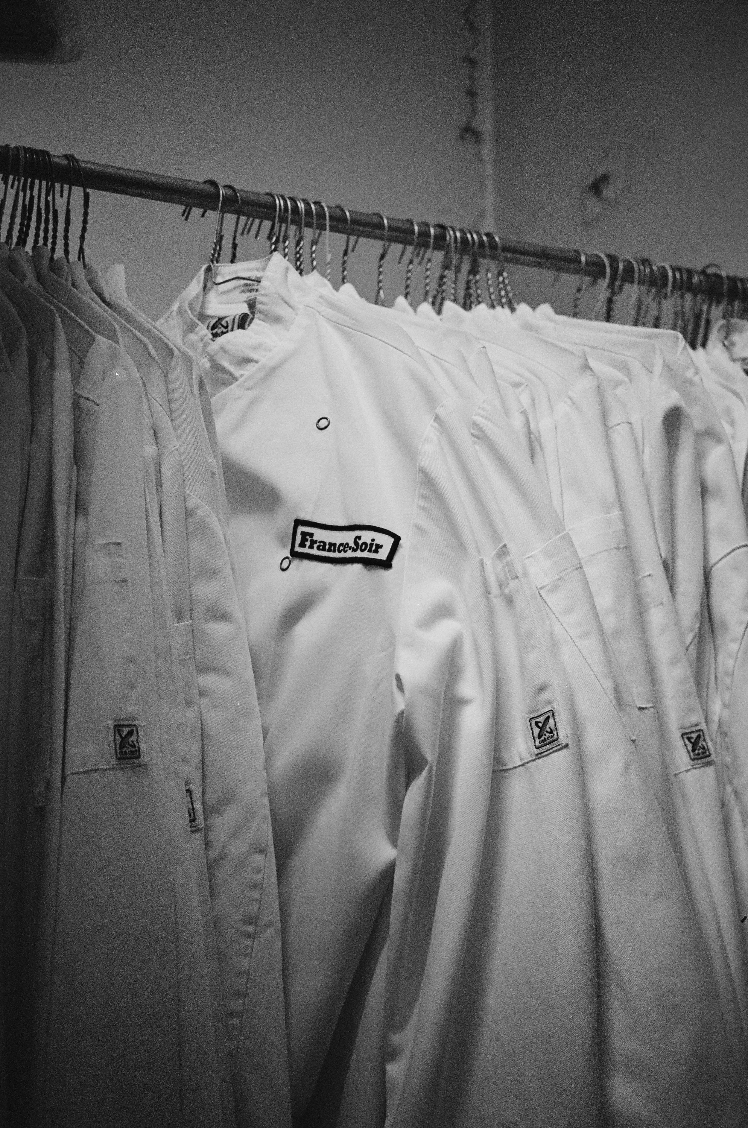 A row of white martial arts uniforms hanging on a metal clothing rack, with a patch that says 'France-Soir' on some of the uniforms.