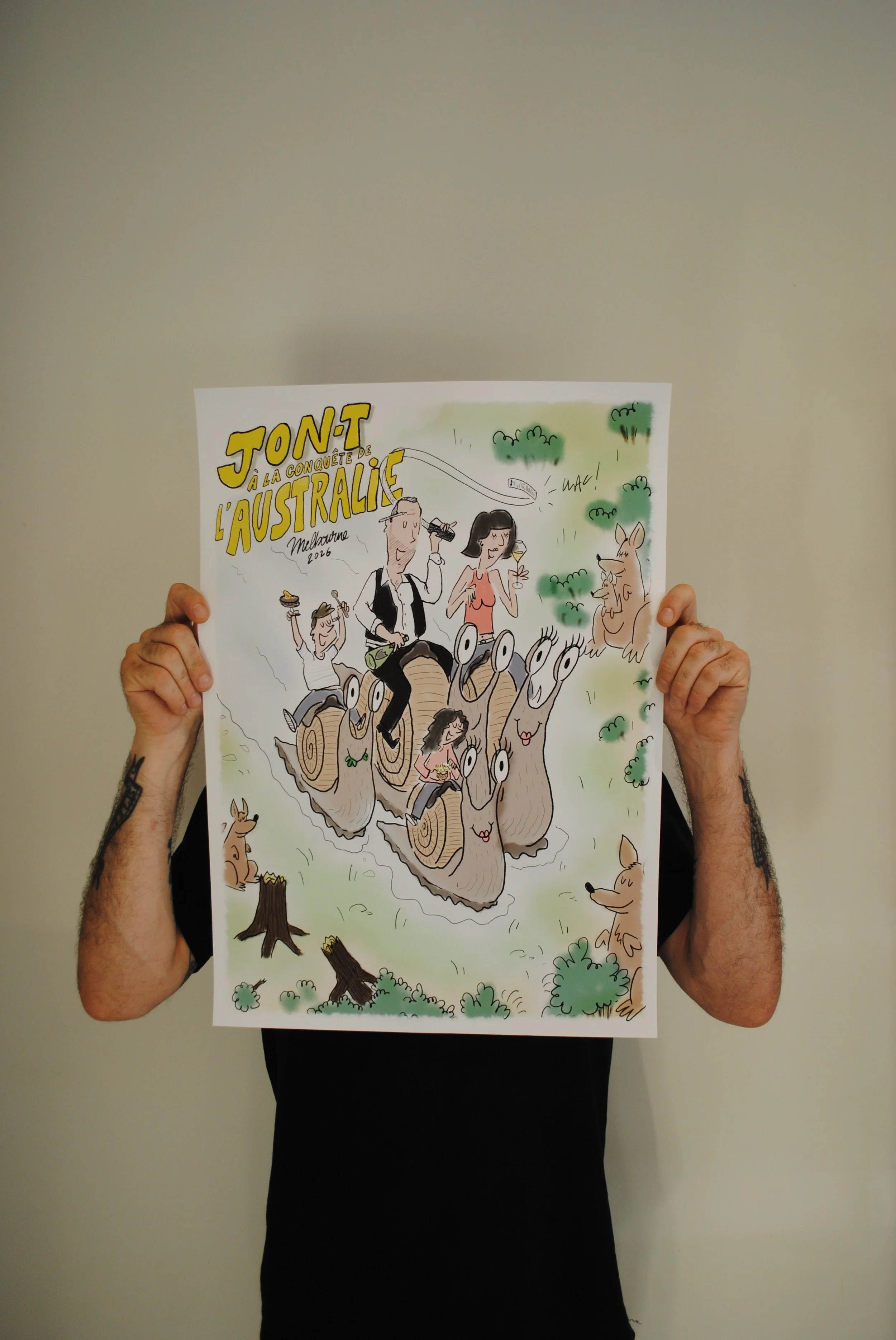 Person holding a colorful cartoon poster about Australia, featuring animals and scenery, in front of a plain wall.