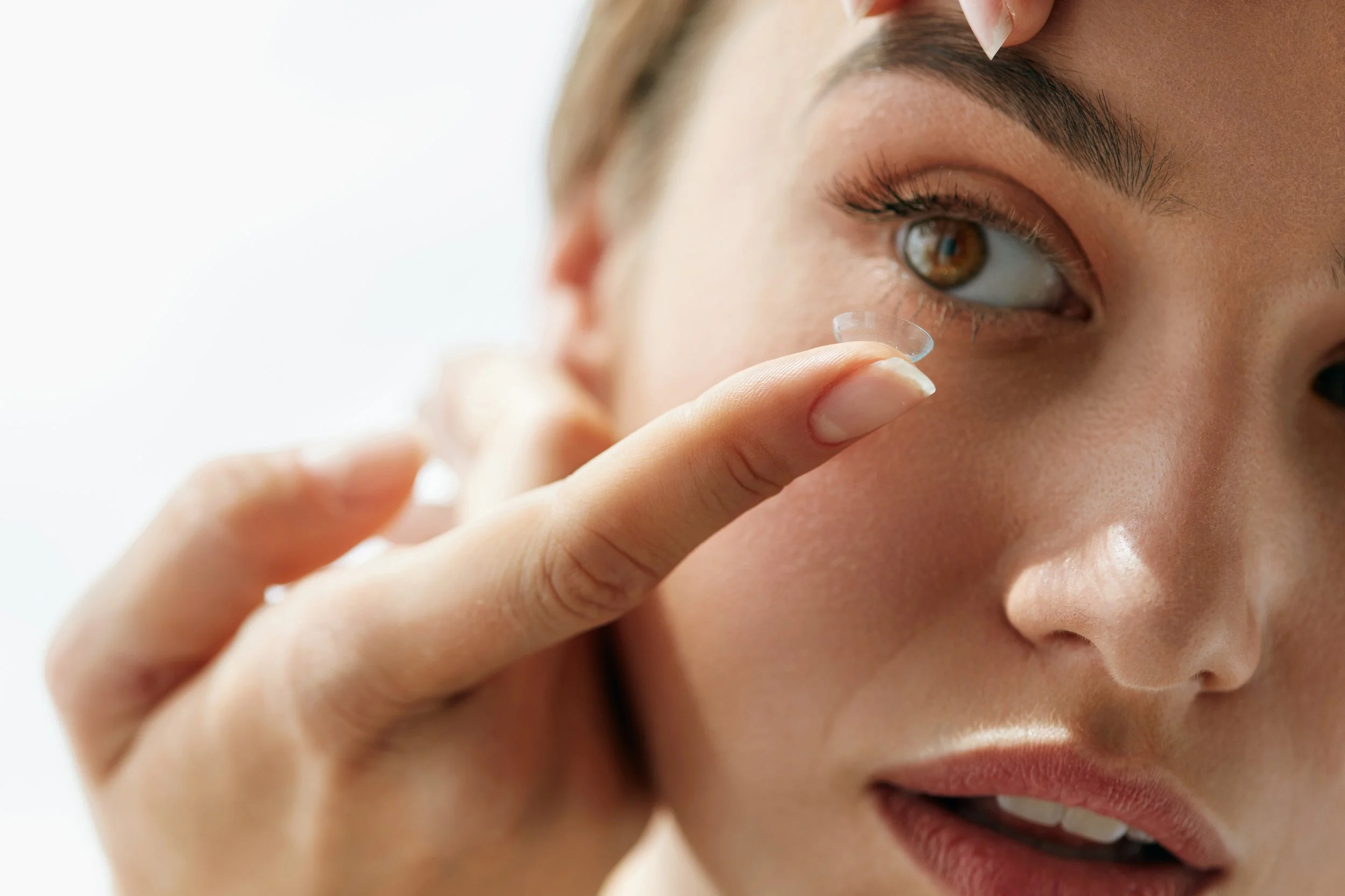 Close-up of a person putting in contact lenses into their eye.
