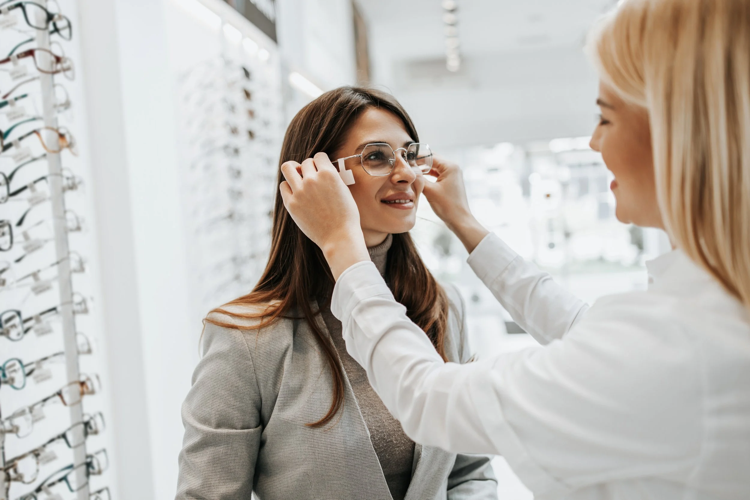 Optician fitting glasses onto a woman's face in an optical store.