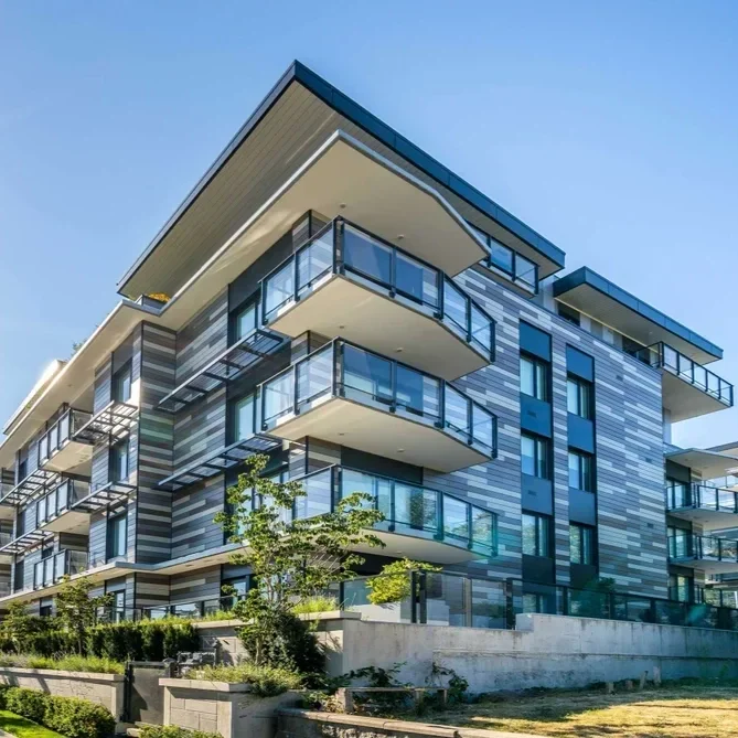 Modern multi-story apartment building with glass balconies and a striped exterior, surrounded by greenery.