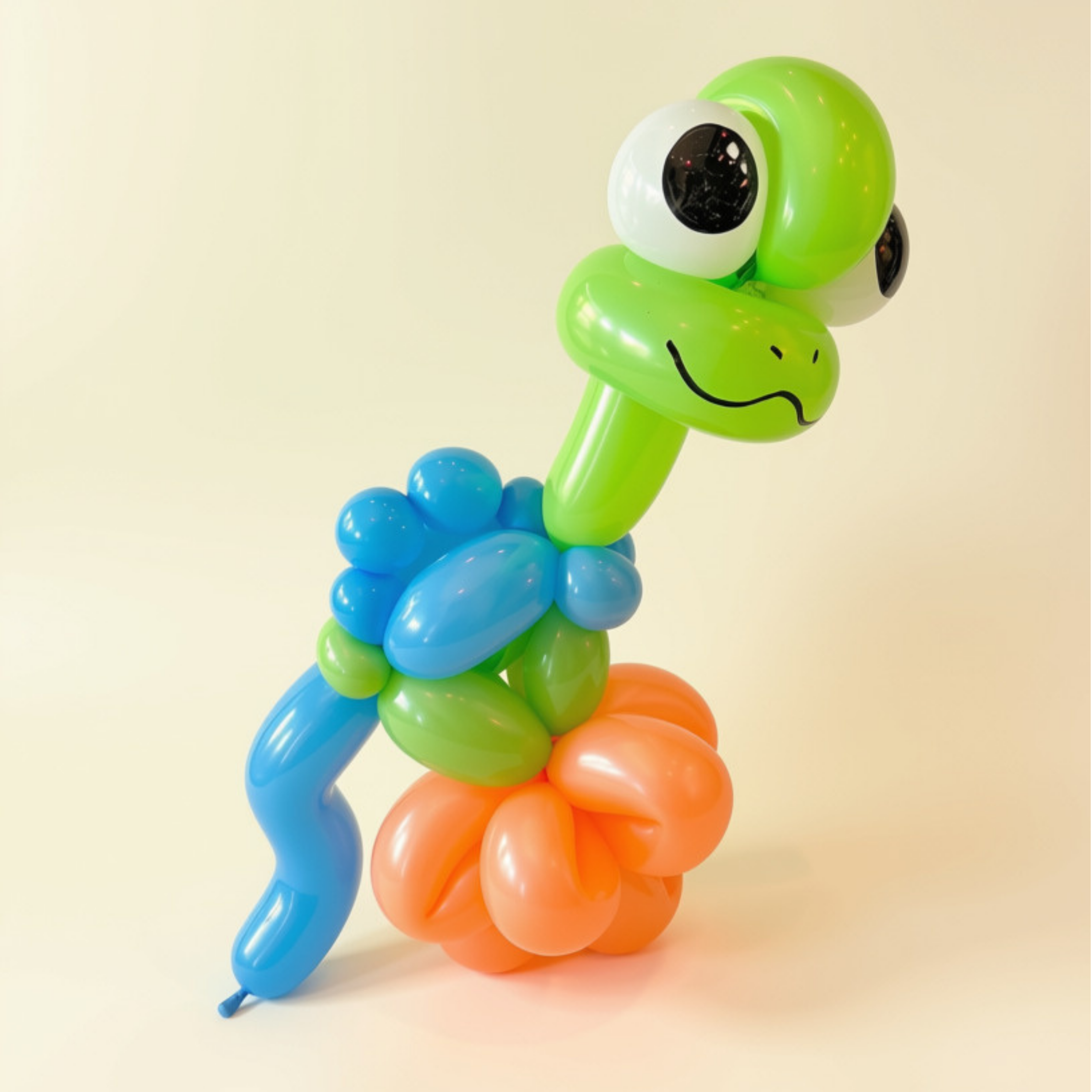 Colorful balloon sculpture of a baby dinosaur with a cartoon face and large eyes, made of various balloons in blue, green, orange, and white, set against a plain cream background.
