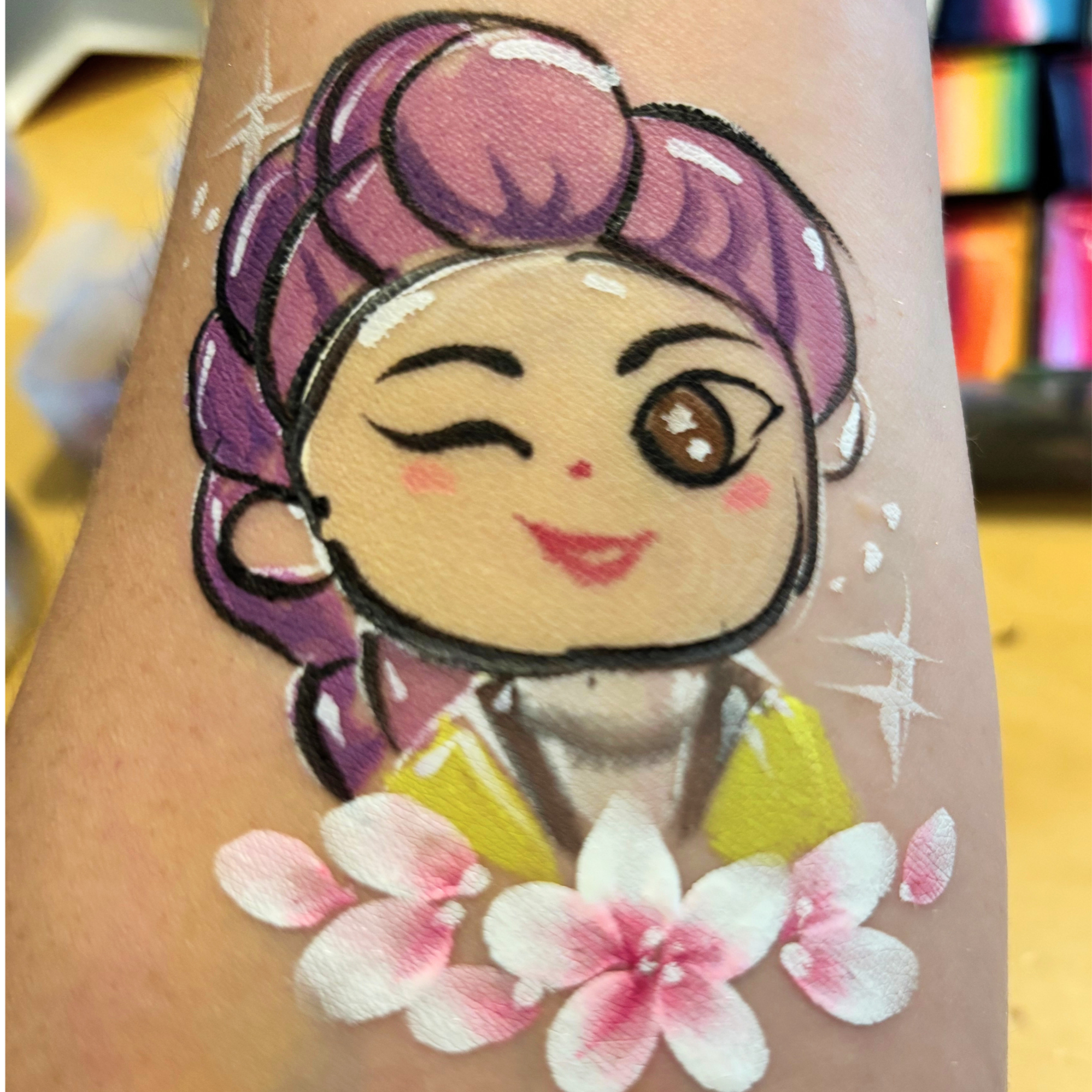Close-up of a colorful tattoo of a cartoon girl with purple hair, a pink headband, and bright eyes, on someone’s skin.