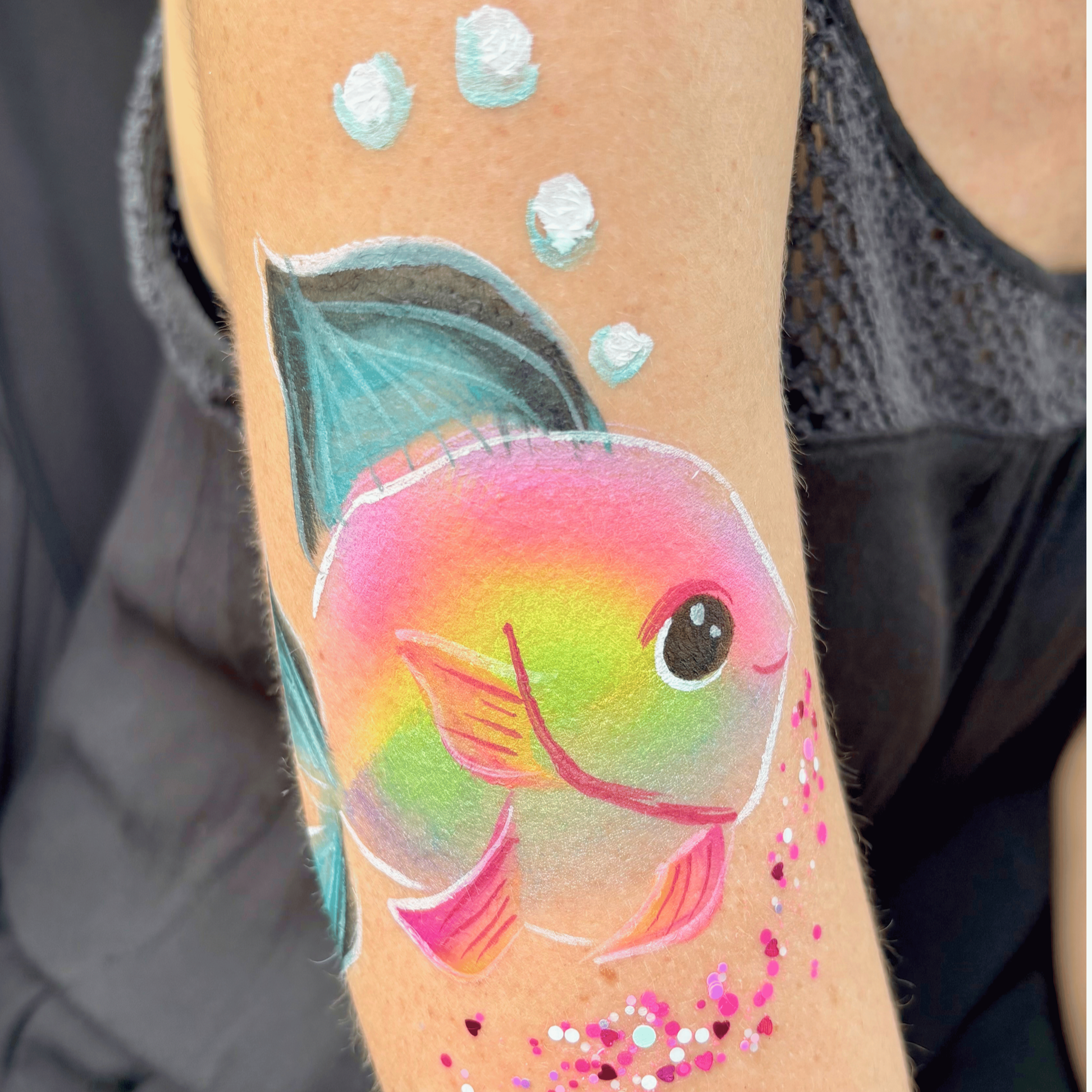 Colorful rainbow with a smiling face, stars, and dots on skin, likely a tattoo or face paint.
