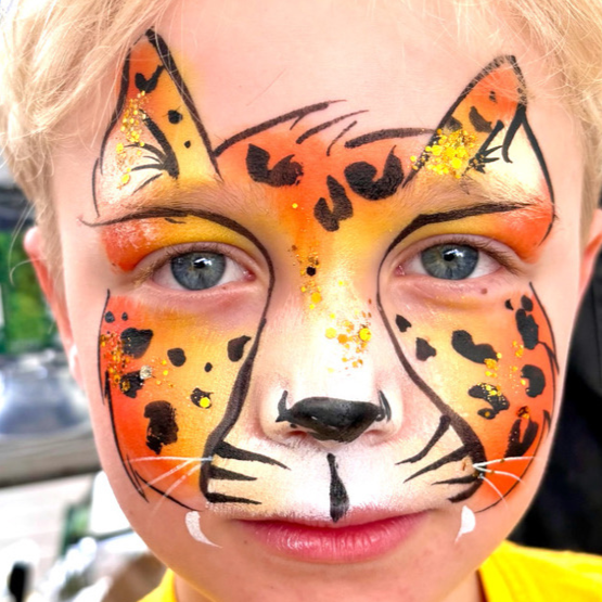 Child with tiger face paint and glitter, featuring orange, black, and white colors, with facial features outlined in black.
