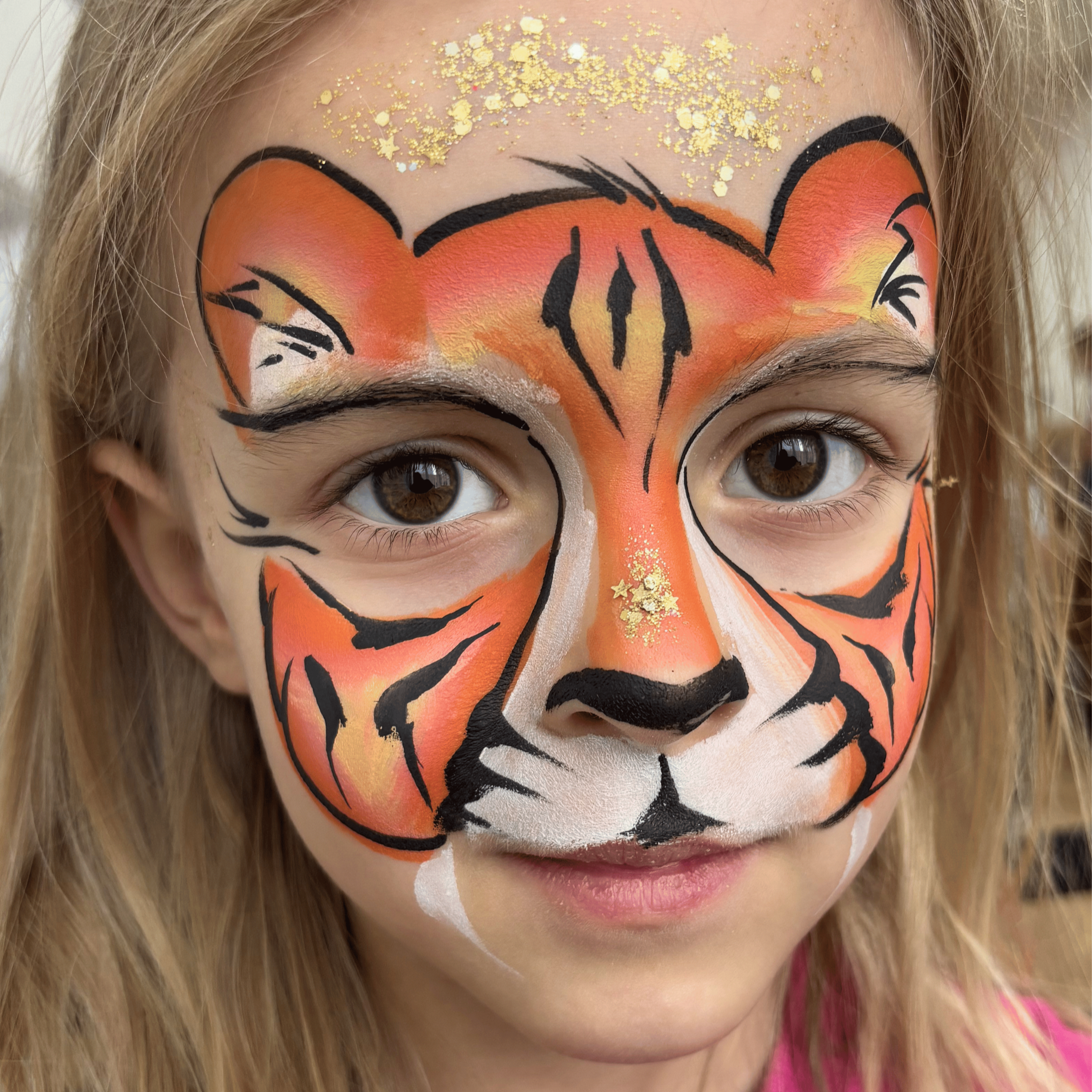 Close-up of a person's face with detailed tiger face paint, including orange, white, and black colors, and glitter on the forehead.
