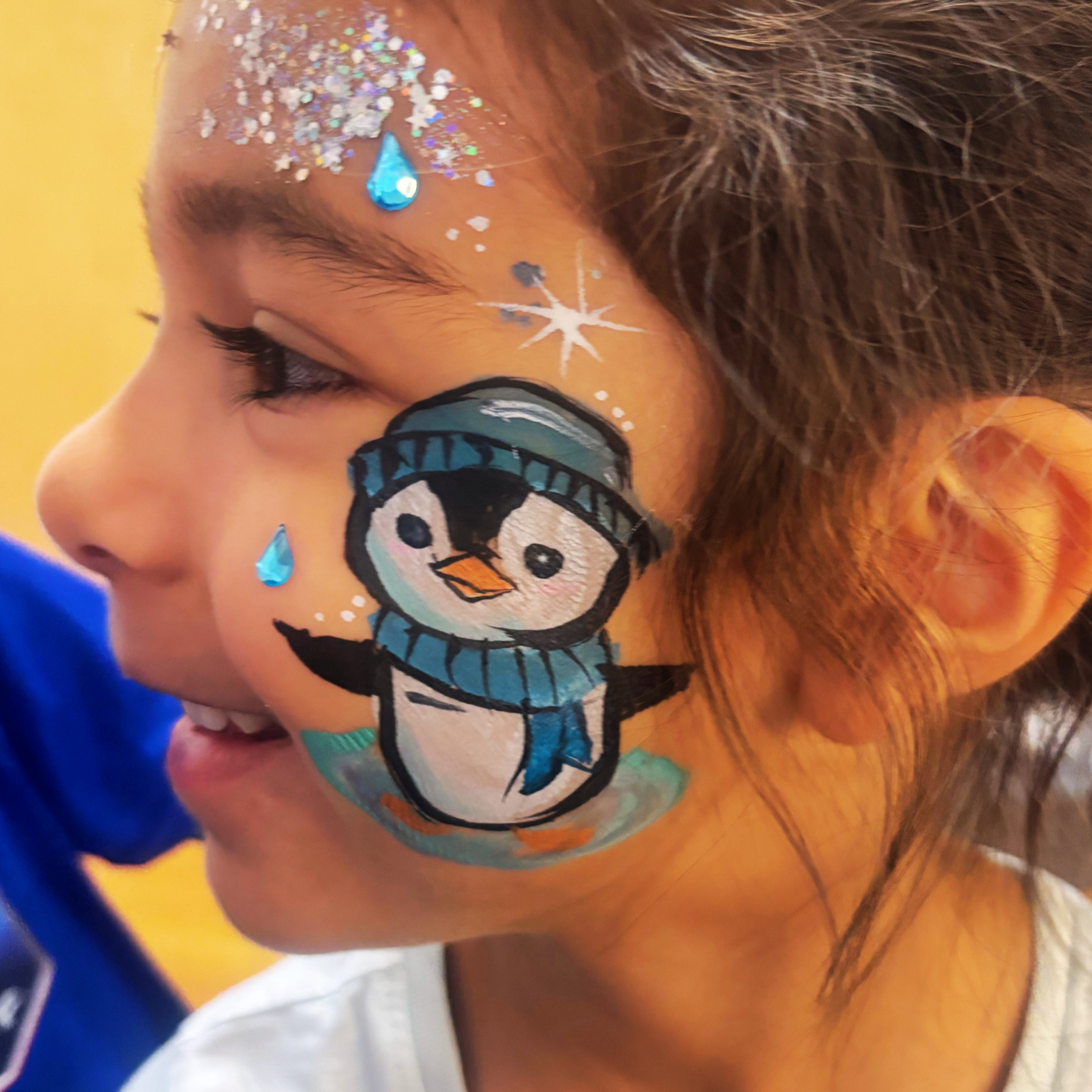 A child's face with face paint of a snowman and glitter around the eye; the snowman has a blue hat and carrot nose, and there are snowflake and teardrop-shaped glitter decorations.
