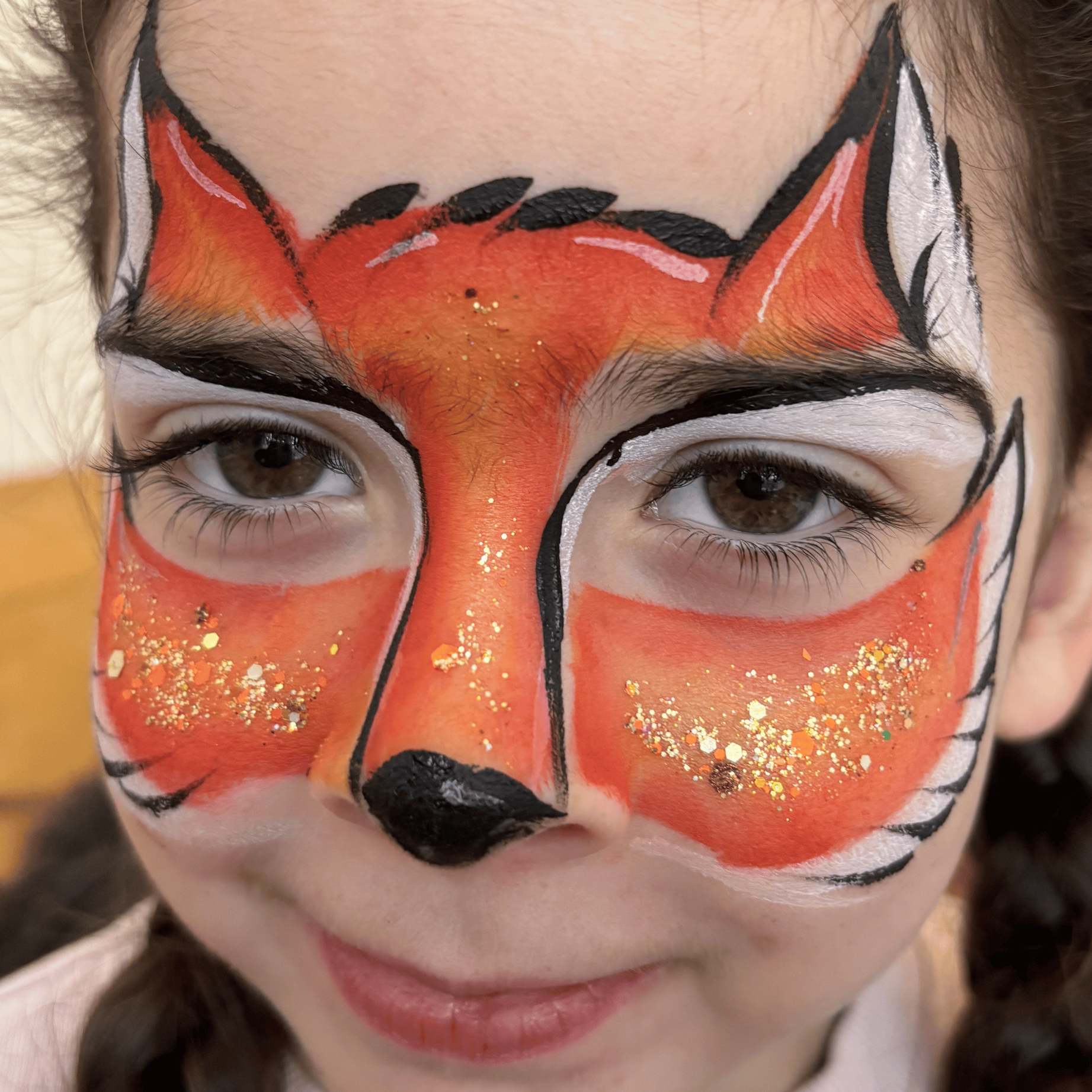 Close-up of a person's face with Halloween or face paint makeup resembling a clown or bones, featuring black, white, orange, and glitter accents, covering the face and framing the eyes.