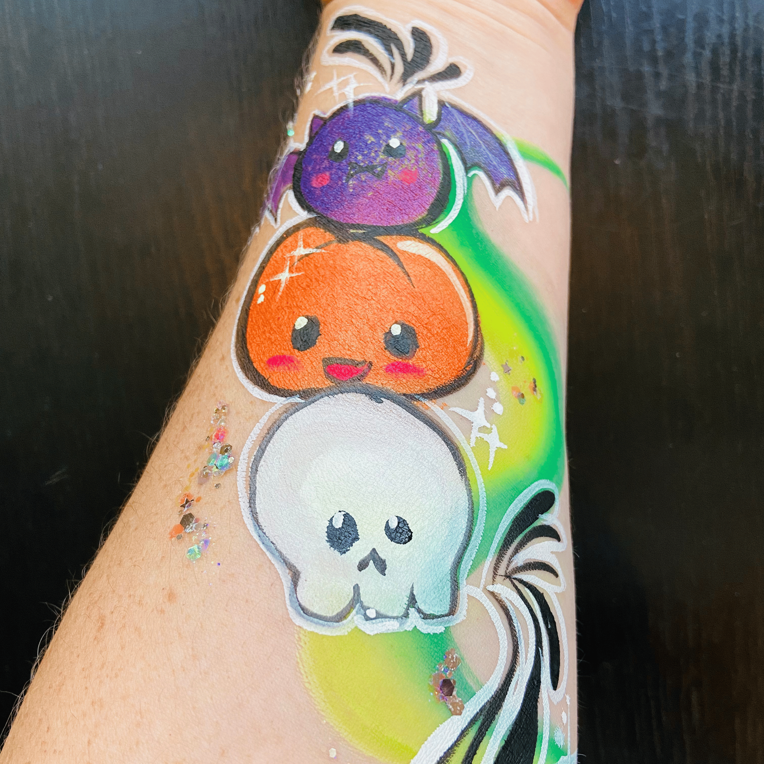 Close-up of colorful halloween face paint of a cartoon bat, pumpkin, and skull