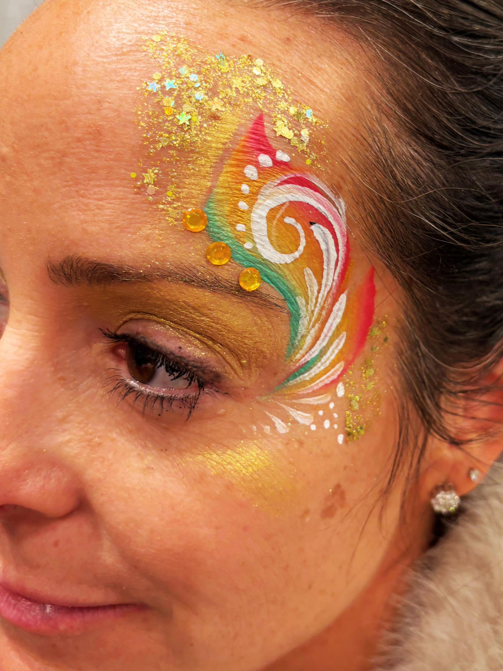 Close-up of a person's face with colorful, glittery face paint and decorative rhinestones.