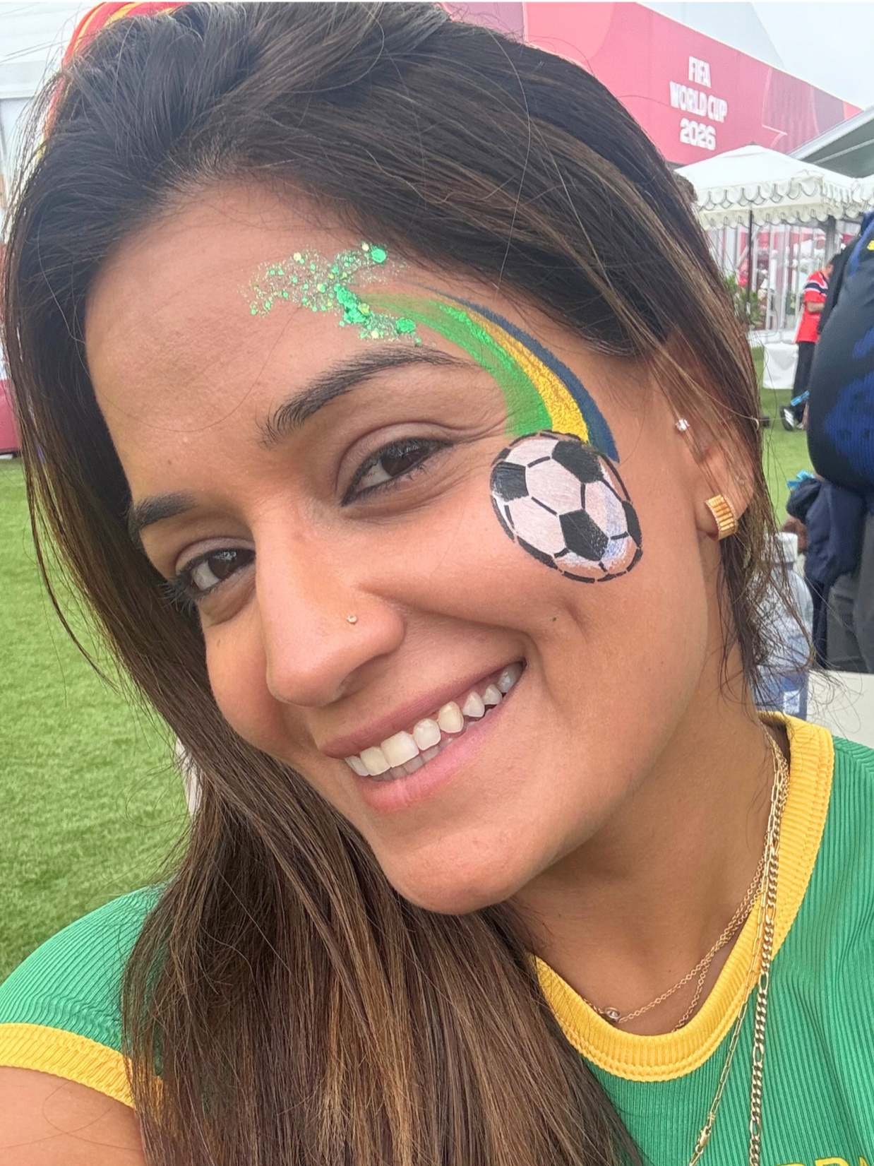 A smiling woman with face paint of a soccer ball and rainbow, at the FIFA World Cup 2026 event.