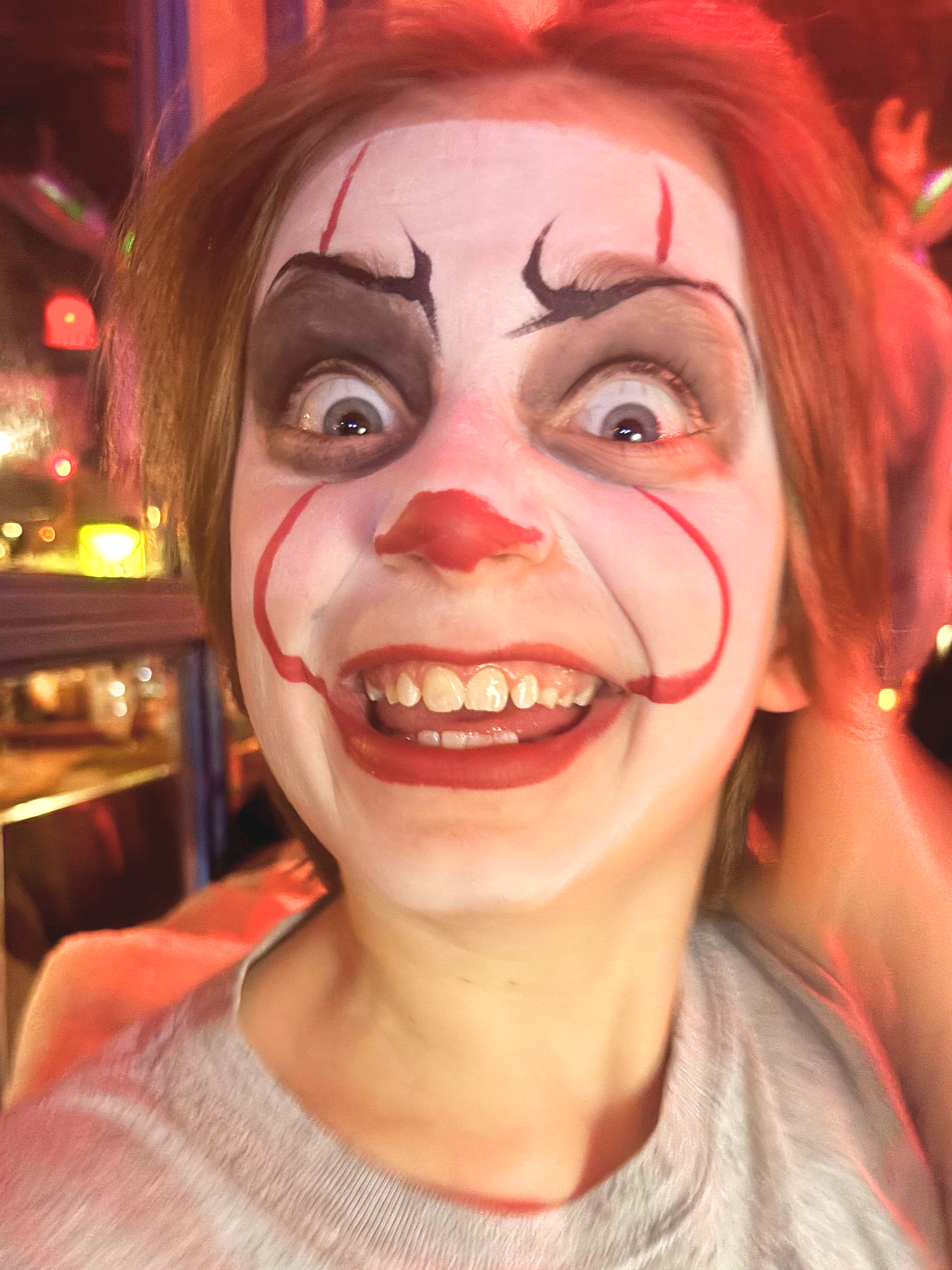 A person with clown makeup and face paint, smiling with wide eyes.