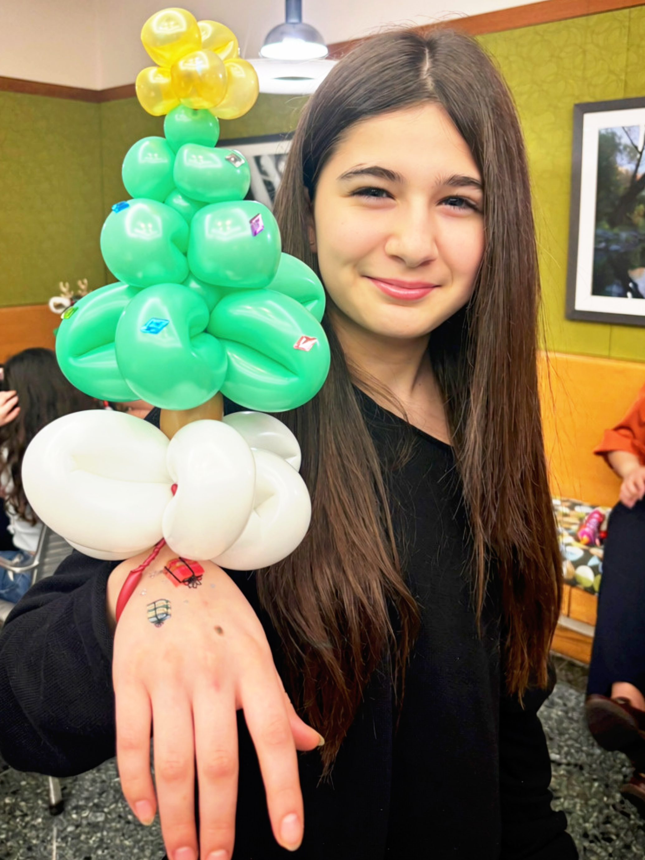 A young woman with long brown hair smiling and showing her bracelet of a balloon Christmas tree