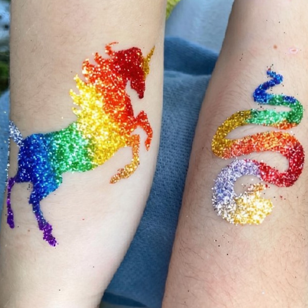 Temporary rainbow-colored tattoos of a unicorn and a snake covered in glitter on arms.