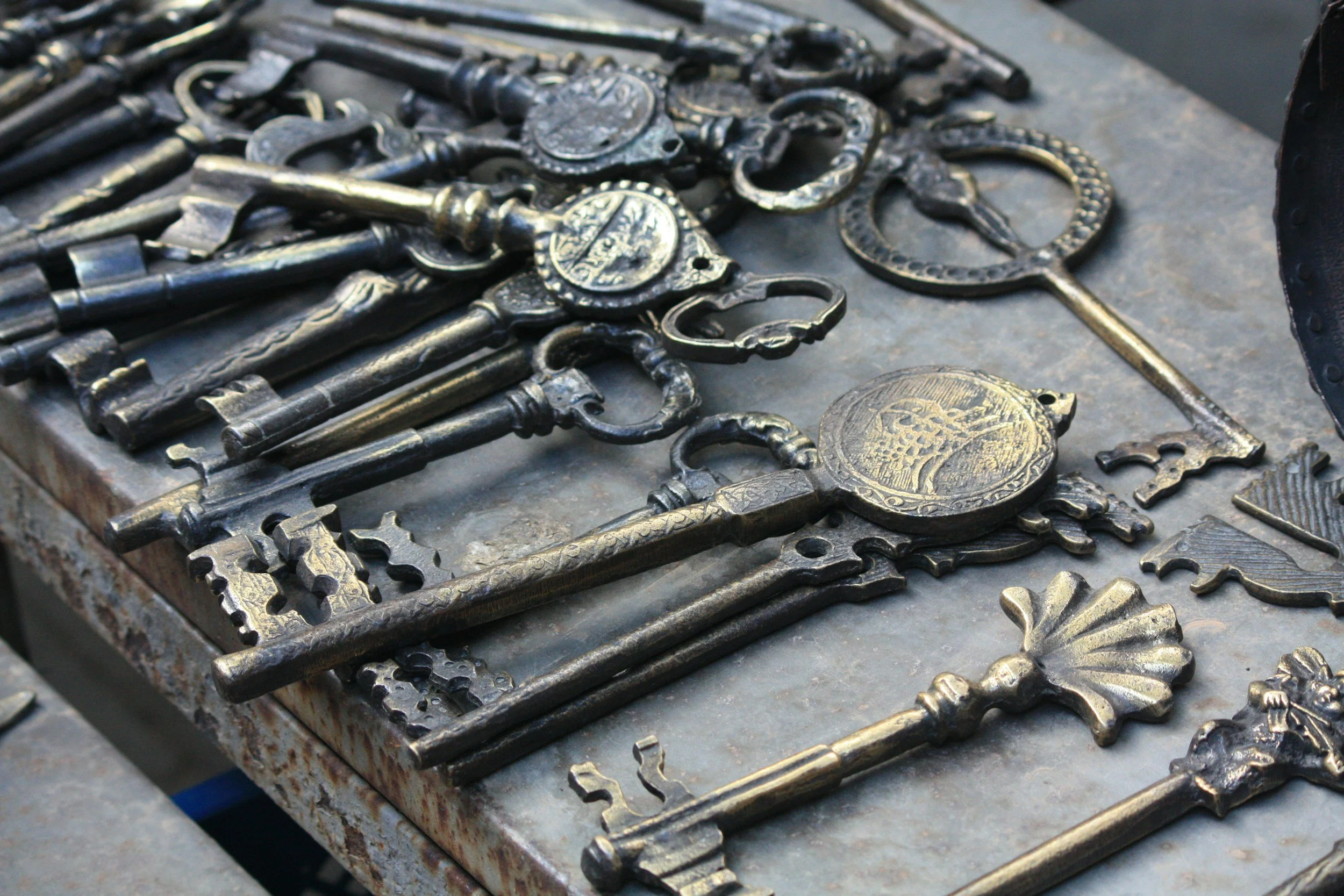 A collection of vintage metal keys and keychains lying on a metal surface.