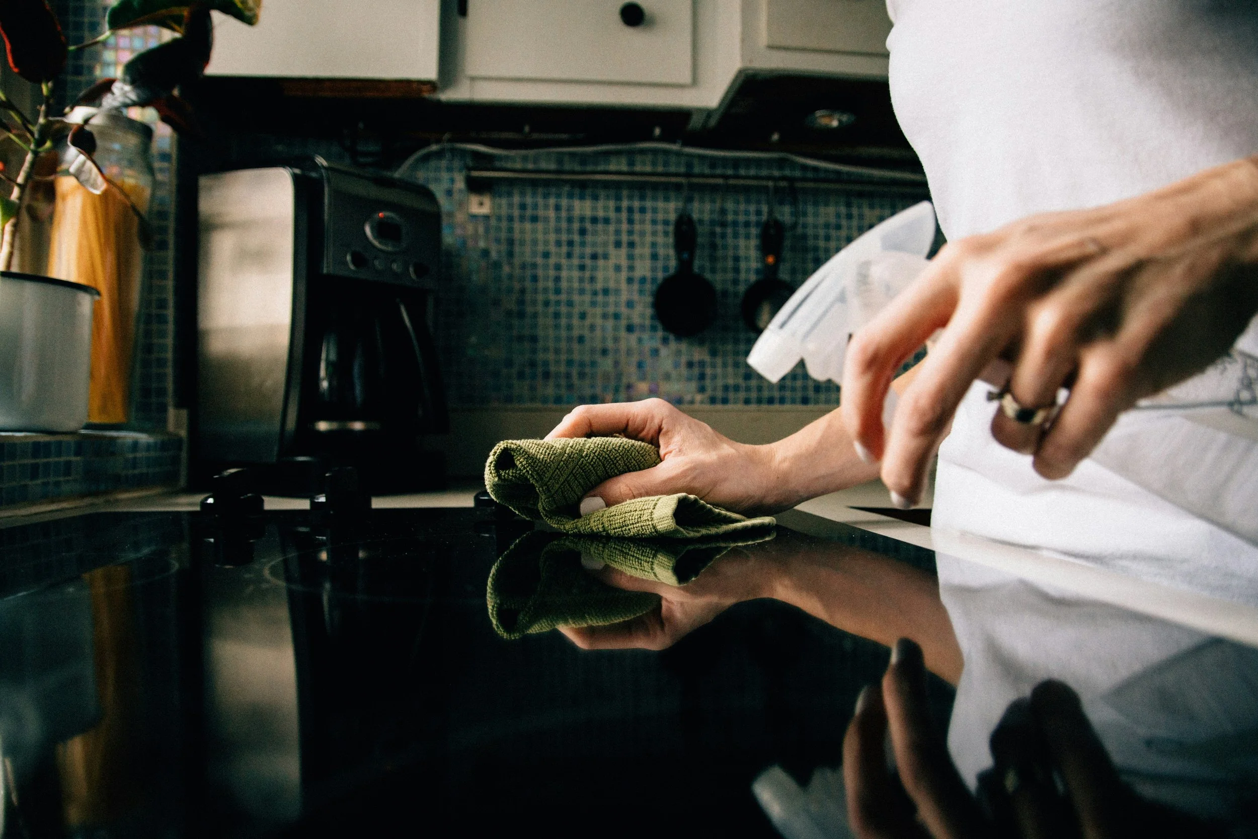 Person wiping a black kitchen countertop with a green cloth.