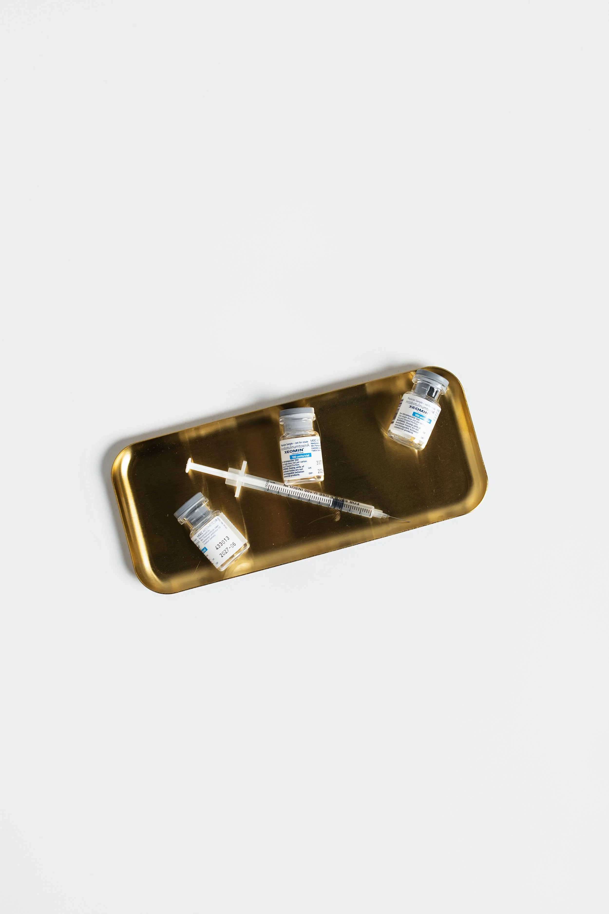 Medical tray with three syringes of neuromodulators, neurotoxins, botox, daxxify, dysport, xeomin and vials of medication on a white background.