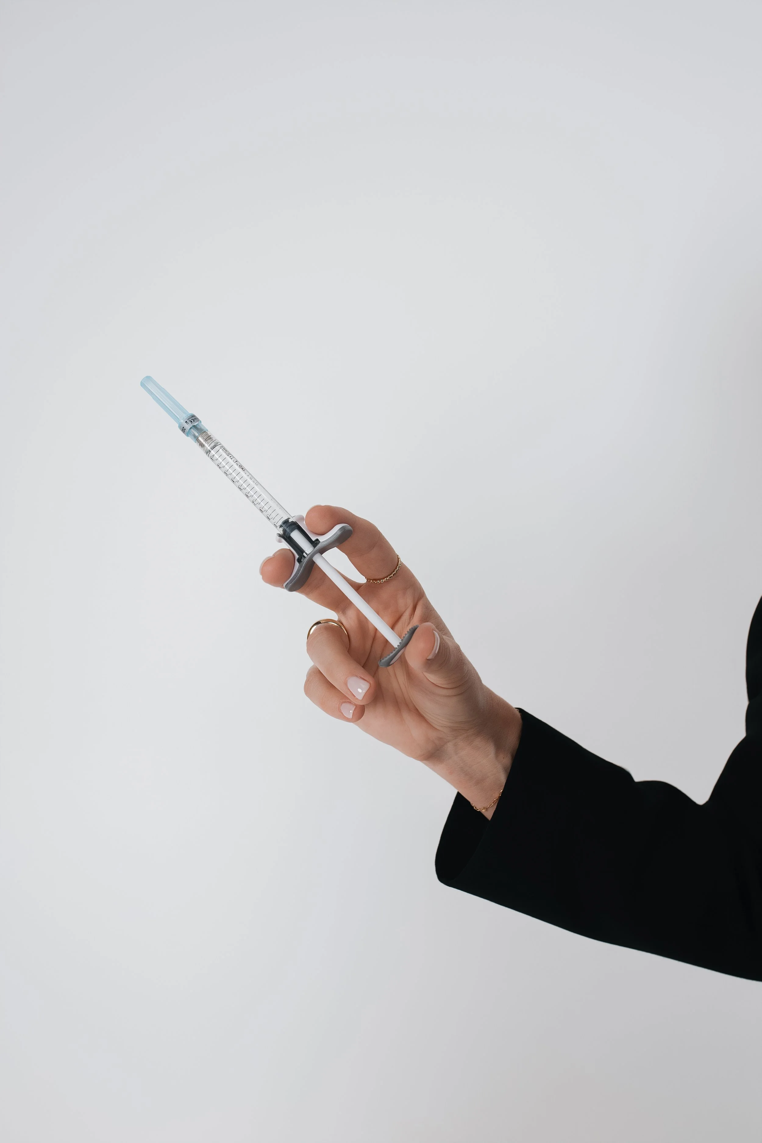 A person in a black sleeve holding a syringe with face filler or lip filler a blue needle tip against a plain white background.